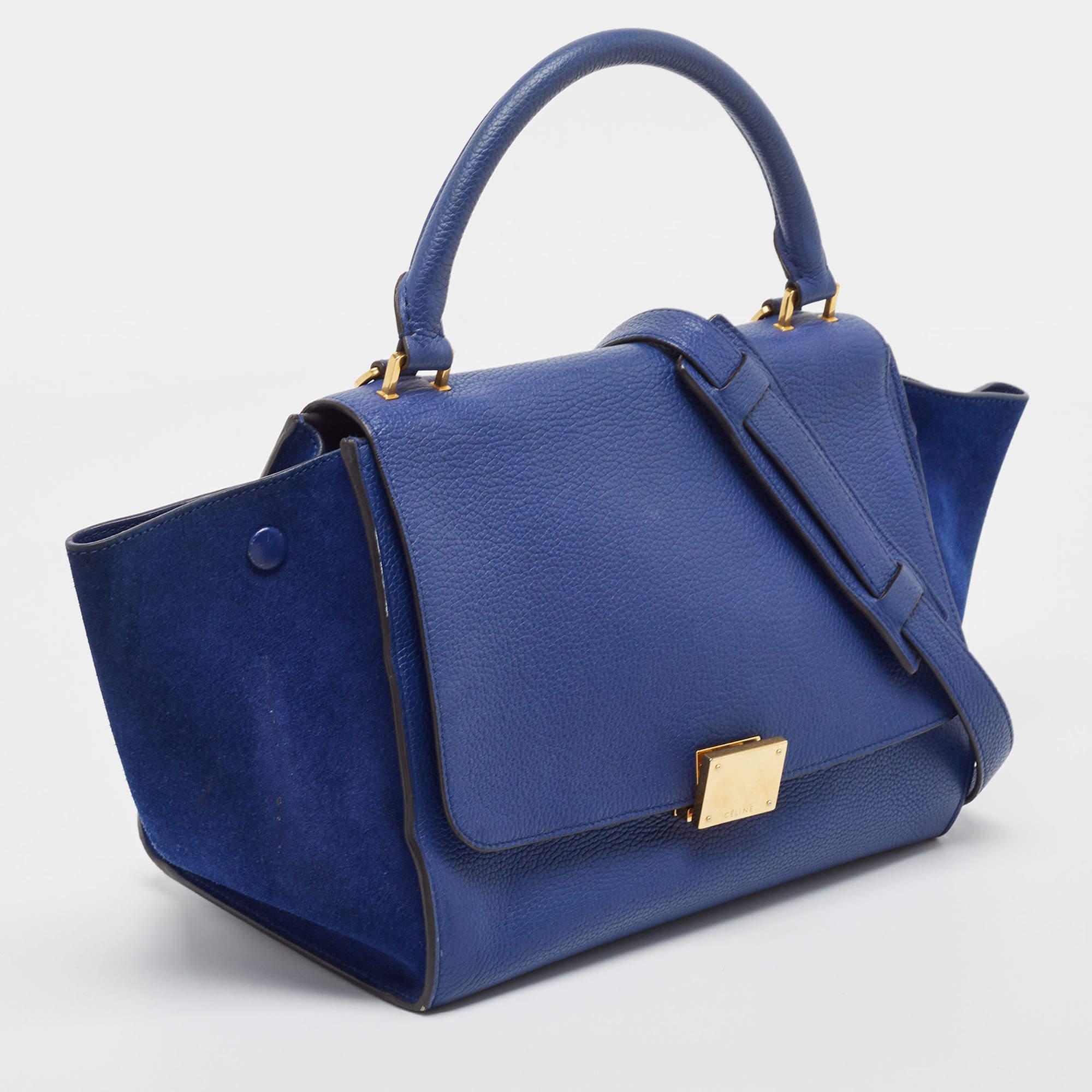 Featuring a simple yet luxurious style, this Celine bag is a valuable addition to your closet. Crafted from leather and suede, it is characterized by flappy wings, gold-tone hardware, and a back zipper pocket. The front flap of this blue tote opens