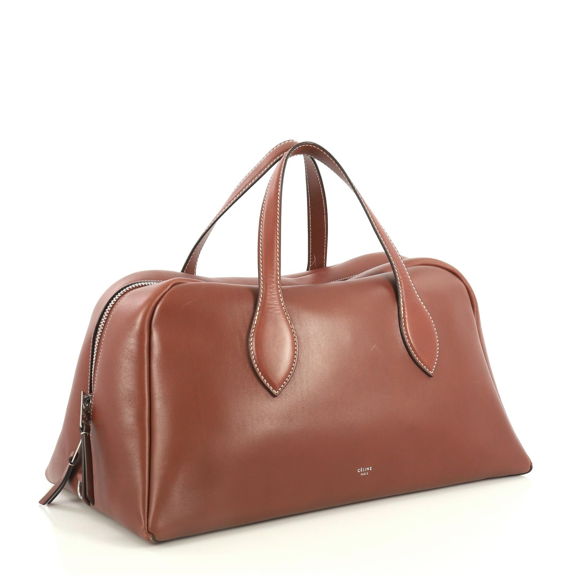 This Celine Bowling Bag Leather Large, crafted from brown leather, features dual flat leather handles and aged silver-tone hardware. Its zip closure opens to a brown suede interior with slip pockets. 

Estimated Retail Price: $3,400
Condition: