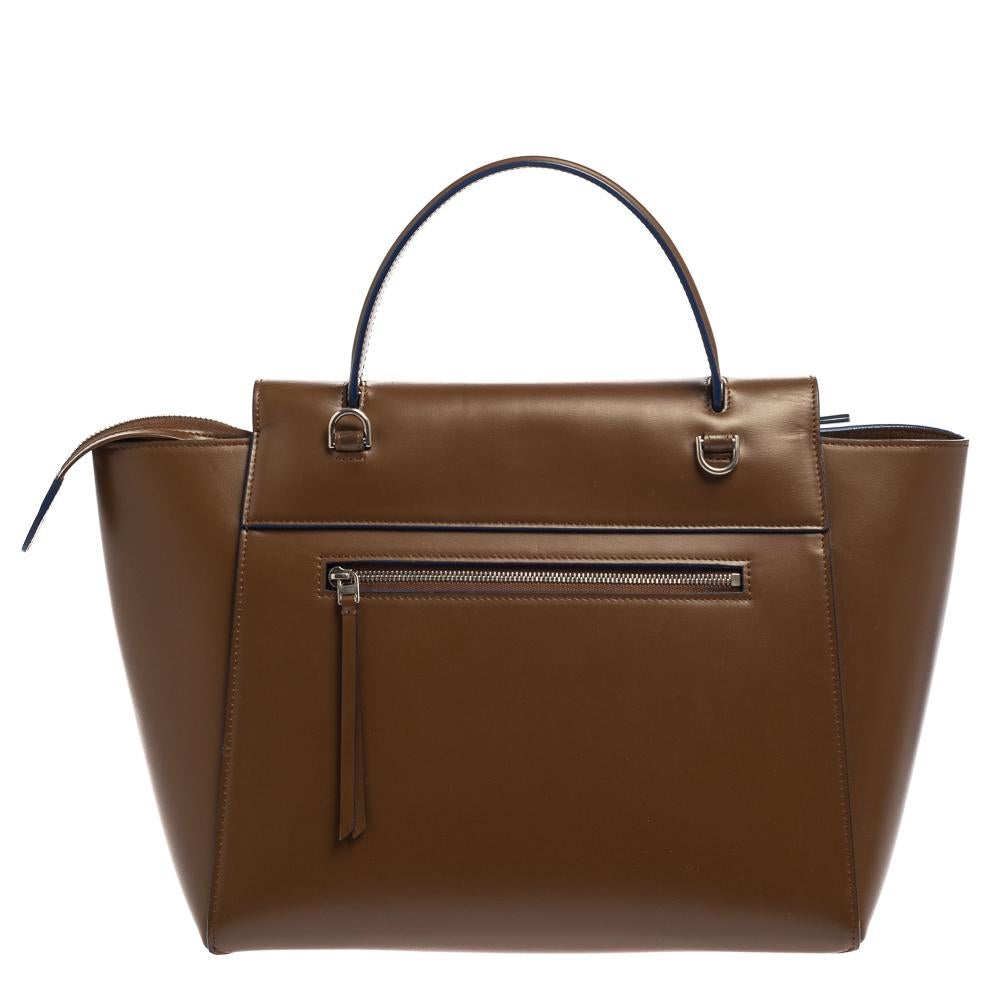 Bags from Celine are symbols of excellent craftsmanship and timeless design. This brown creation has been crafted from leather and styled with a front flap and belt details. It flaunts a single top handle, a zip pocket at the back, and a spacious