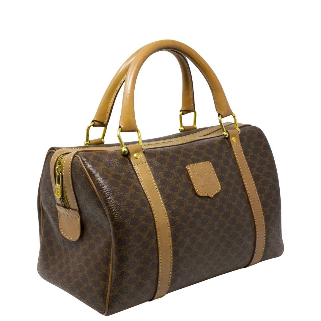 Super cute small Celine Boston Top Handle bag crafted in Celine monogram coated canvas with caramel brown leather trimmings and logo plate to the front, dual rolled top handles, and gold-tone hardware. The zipper opens up to a tonal interior lining