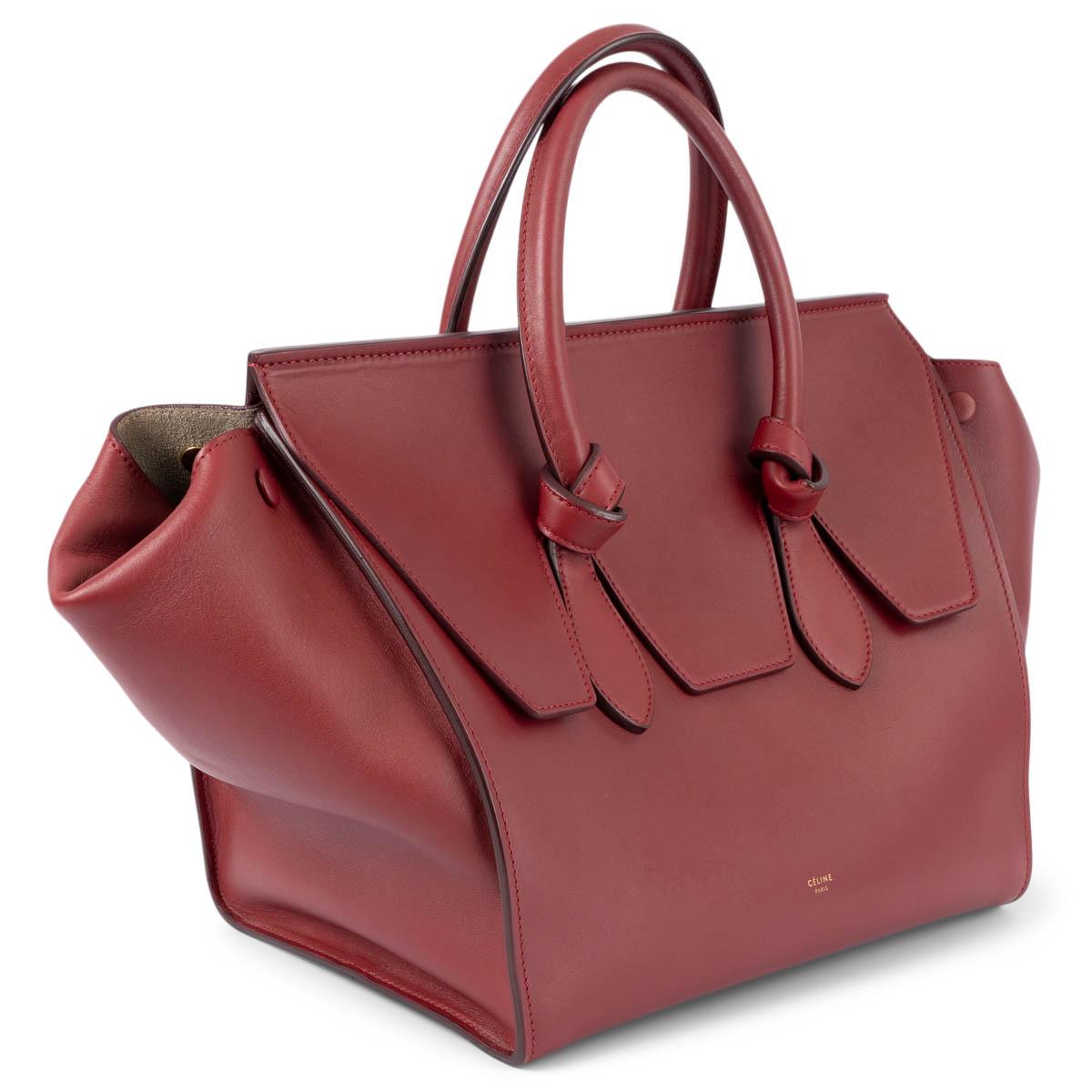 100% authentic Céline Small Tie bag in smooth burgundy calfskin and gold-tone hardware. The design features knotted handles and wide side gussets with strap closure. Lined in light grey suede with one zipper and two patch pockets against the back.