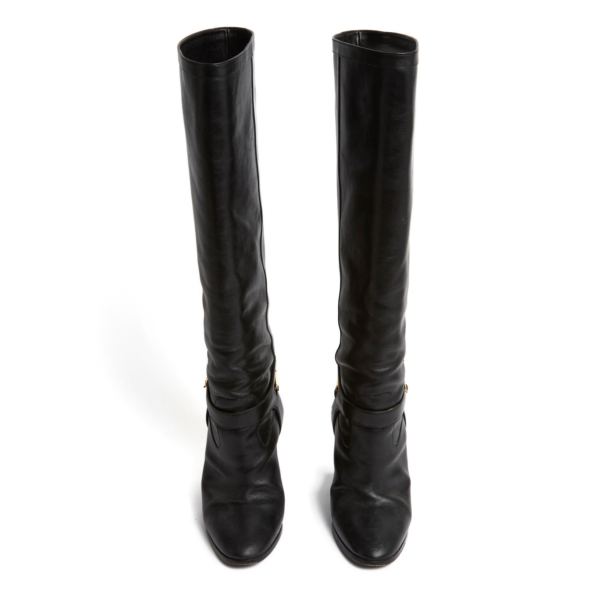 Celine boots by Hedi Slimane in black leather with straight heel, leather strap lined with equestrian-inspired gold metal, straight shaft, almond toe. Size 40FR, insole 25.7 cm, heel 11 cm, shaft height (from the heel) 42 cm, calf width 20 cm (calf