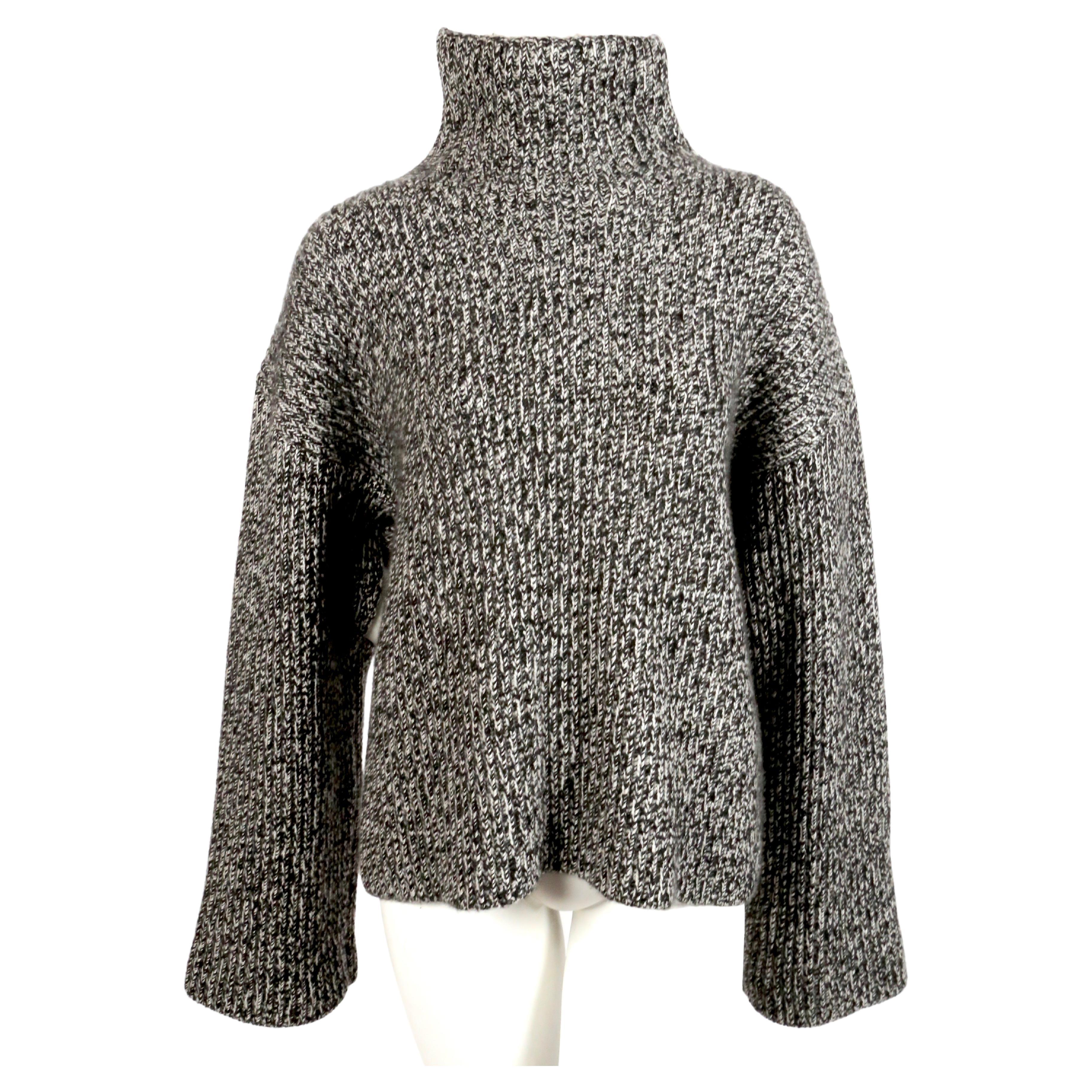 Black and off-white fuzzy cashmere stand-up collar jumper from Celine features a high standing collar, long sleeves with cutouts under arms, a chunky knit and a straight hem. Sweater can be worn similar to a cape with the underarm cutouts. Designed