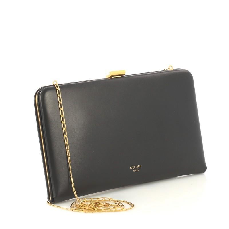 This Celine Clasp Wallet on Chain Leather Large, crafted from black leather, features a chain link strap, framed silhouette, and gold-tone hardware. It opens to an orange leather interior with multiple card slots and slip pocket. 

Estimated Retail