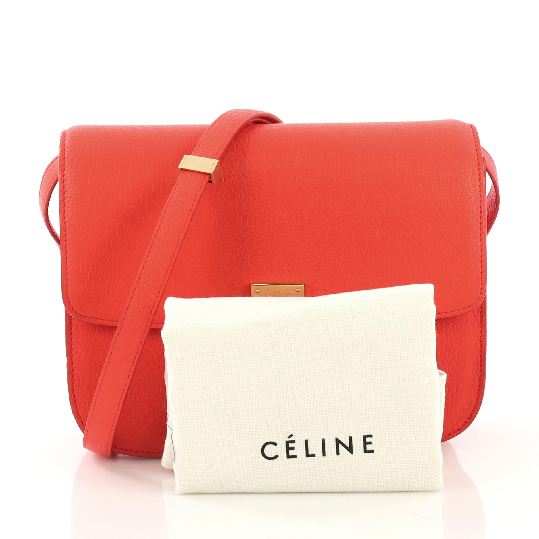 This Celine Classic Box Bag Grainy Leather Medium, crafted from red leather, features a long adjustable strap and gold-tone hardware. Its push-tab closure opens to a red leather interior with zip compartment and two open compartments with side slip