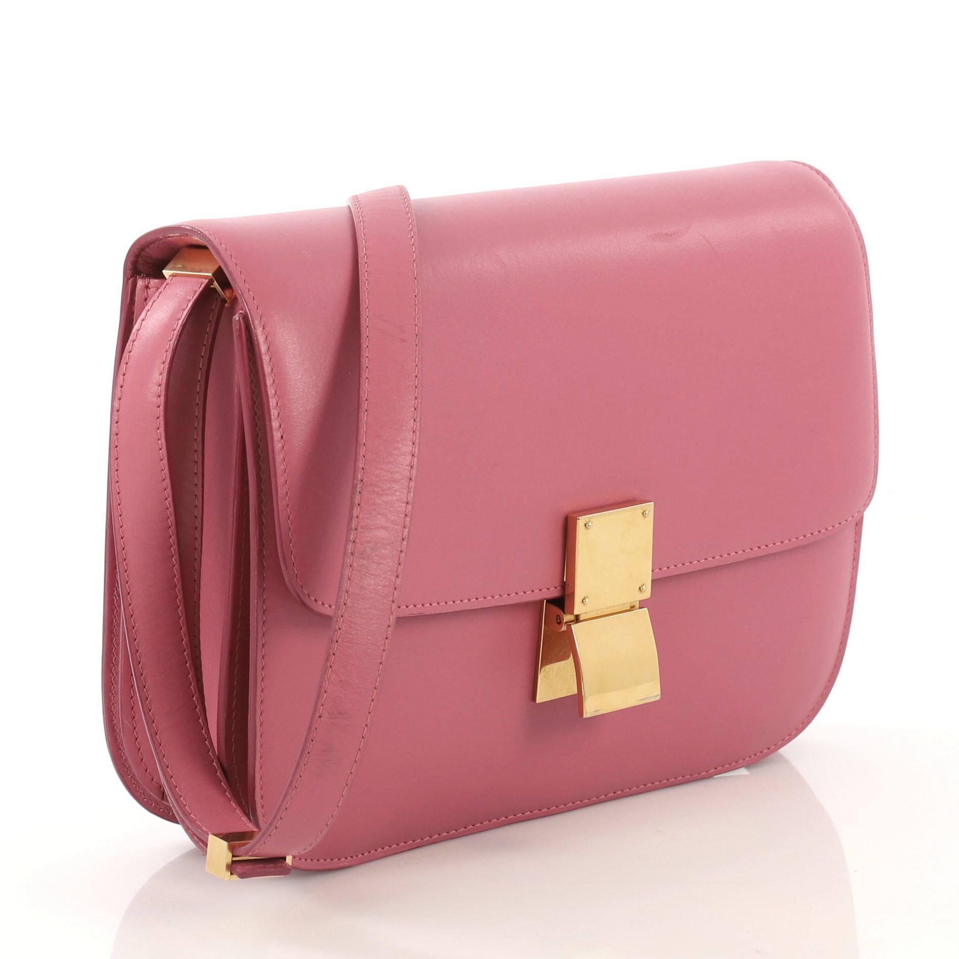 This Celine Classic Box Bag Smooth Leather Medium, crafted from pink smooth leather, features a long adjustable strap and gold-tone hardware. Its push-tab closure opens to a pink leather interior with two open compartments, zip compartment and slip