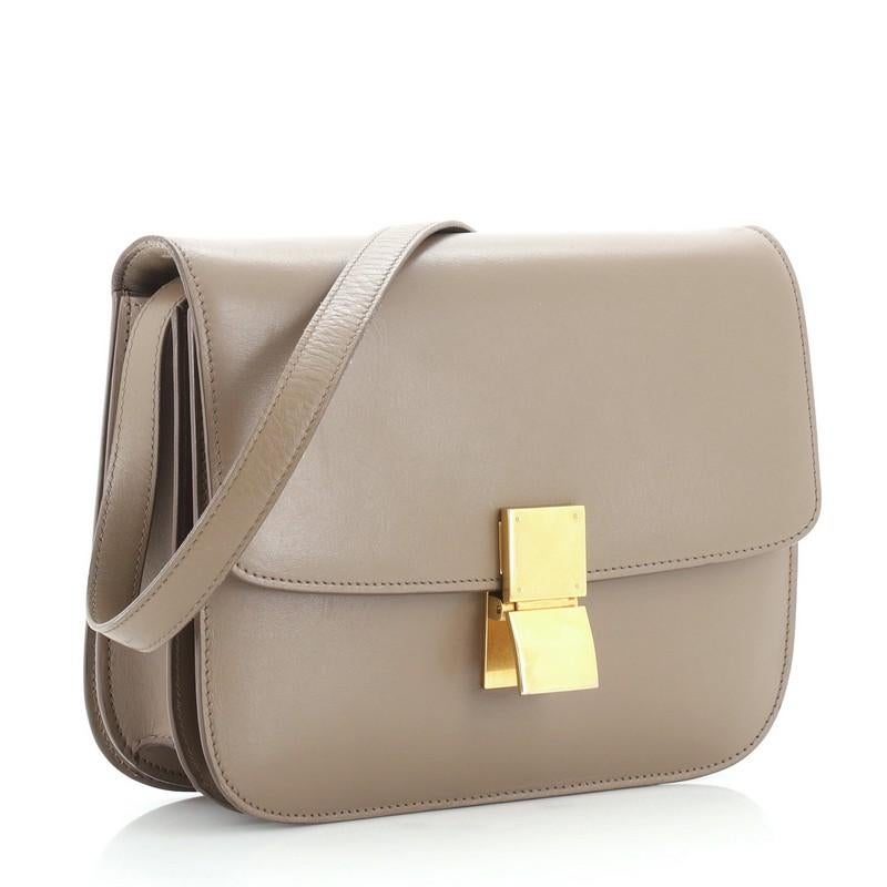 This Celine Classic Box Bag Smooth Leather Medium, crafted from neutral smooth leather, features a long adjustable strap and gold-tone hardware. Its push-tab closure opens to a neutral leather interior with two open compartments, zip compartment and