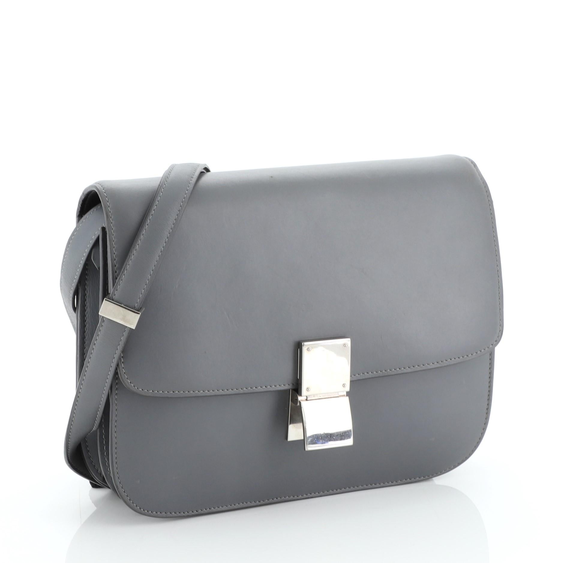 This Celine Classic Box Bag Smooth Leather Medium, crafted from gray smooth leather, features a long adjustable strap and silver-tone hardware. Its push-tab closure opens to a black leather interior with two open compartments, zip compartment and