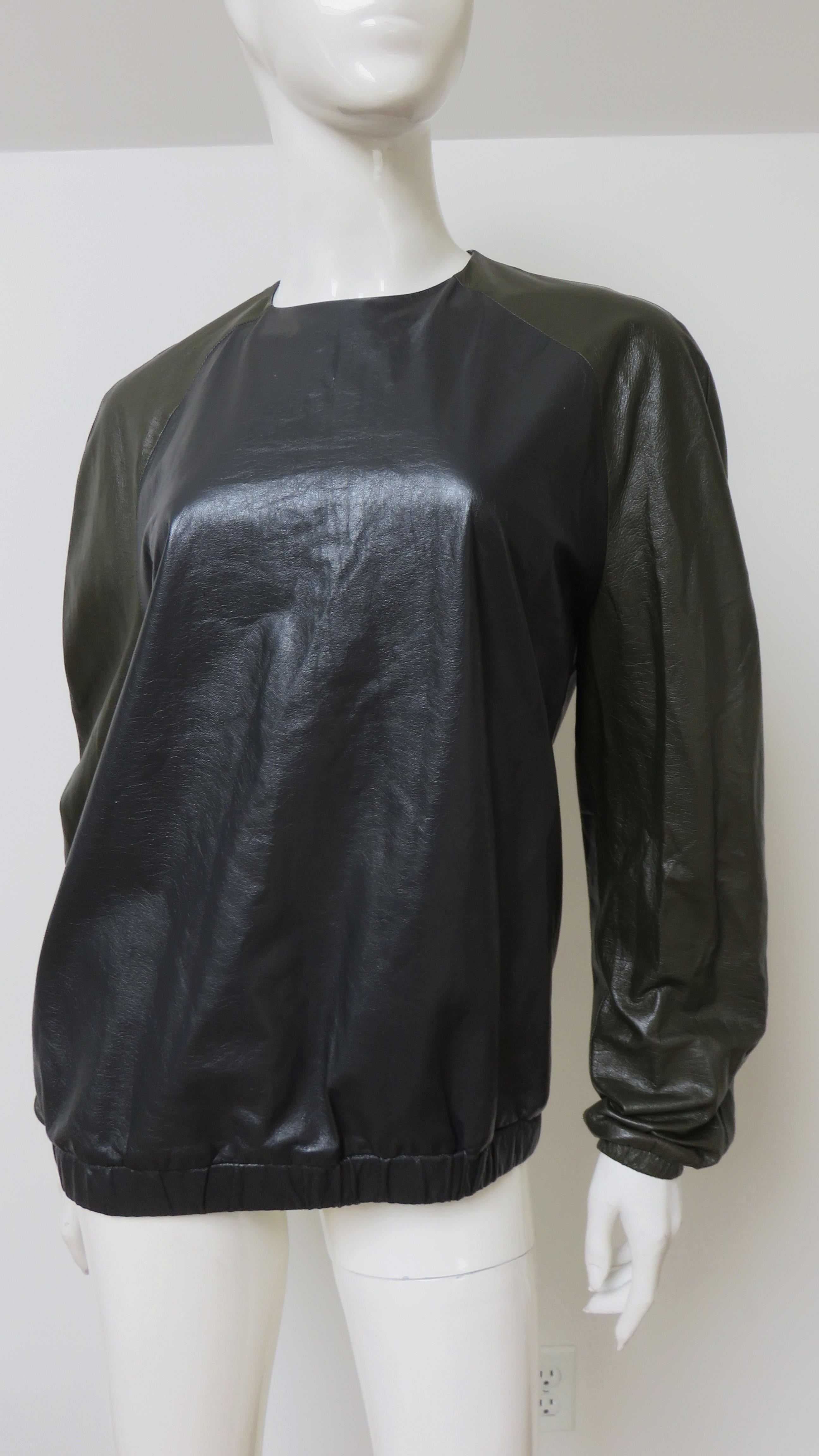 Un top de cuero negro y verde oliva intenso súper chic de Celine. Tiene escote redondo, mangas raglán largas con elástico en los puños y cuerpo blusón con elástico en el bajo.  El cuerpo del top es de cuero negro y las mangas son de cuero verde