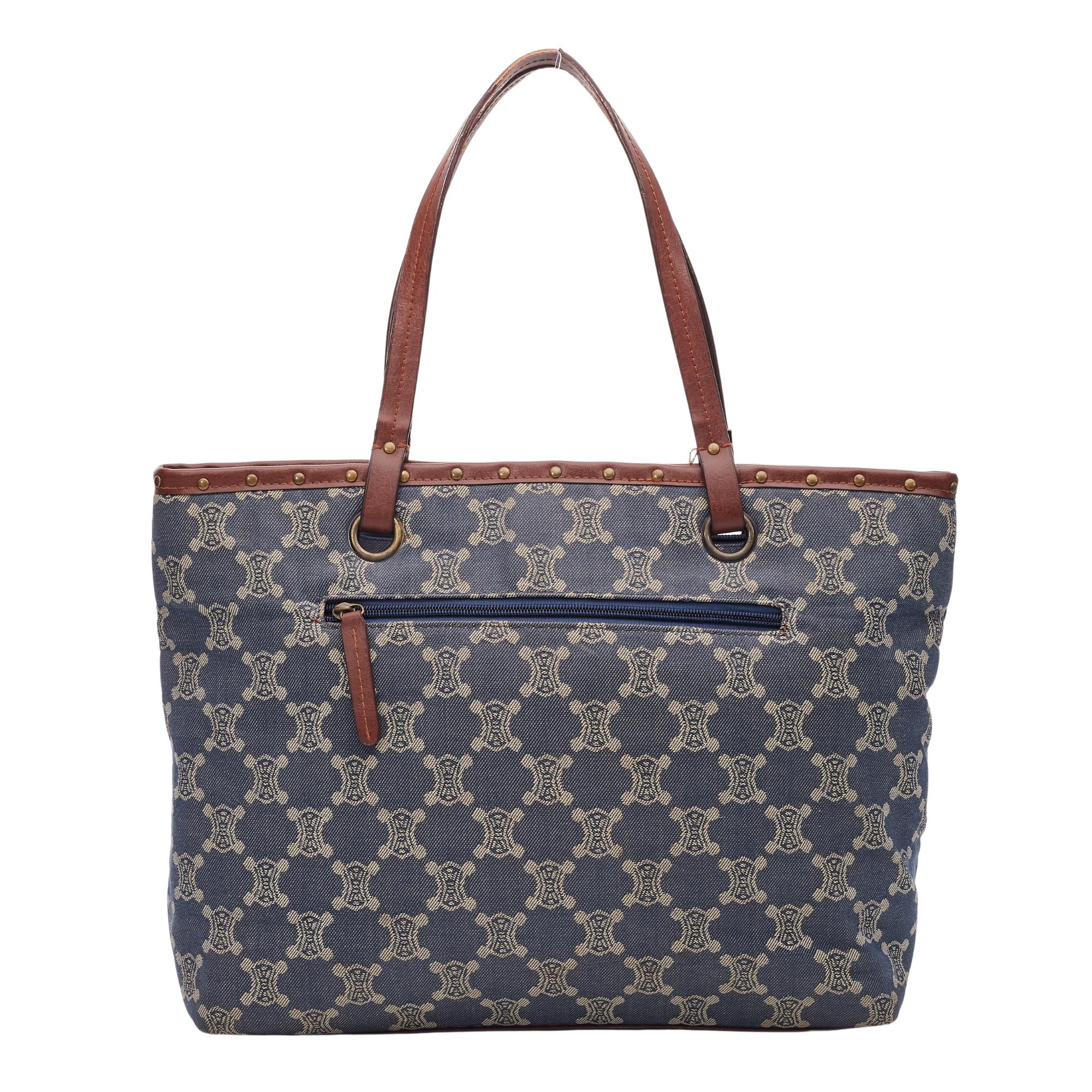 Dark wash blue and creme embroidered denim Céline tote with antiqued gold-tone hardware, brown leather trim, dual flat shoulder straps, stud embellishments throughout, tonal denim interior. single zip pocket at interior wall and open top.

Color: