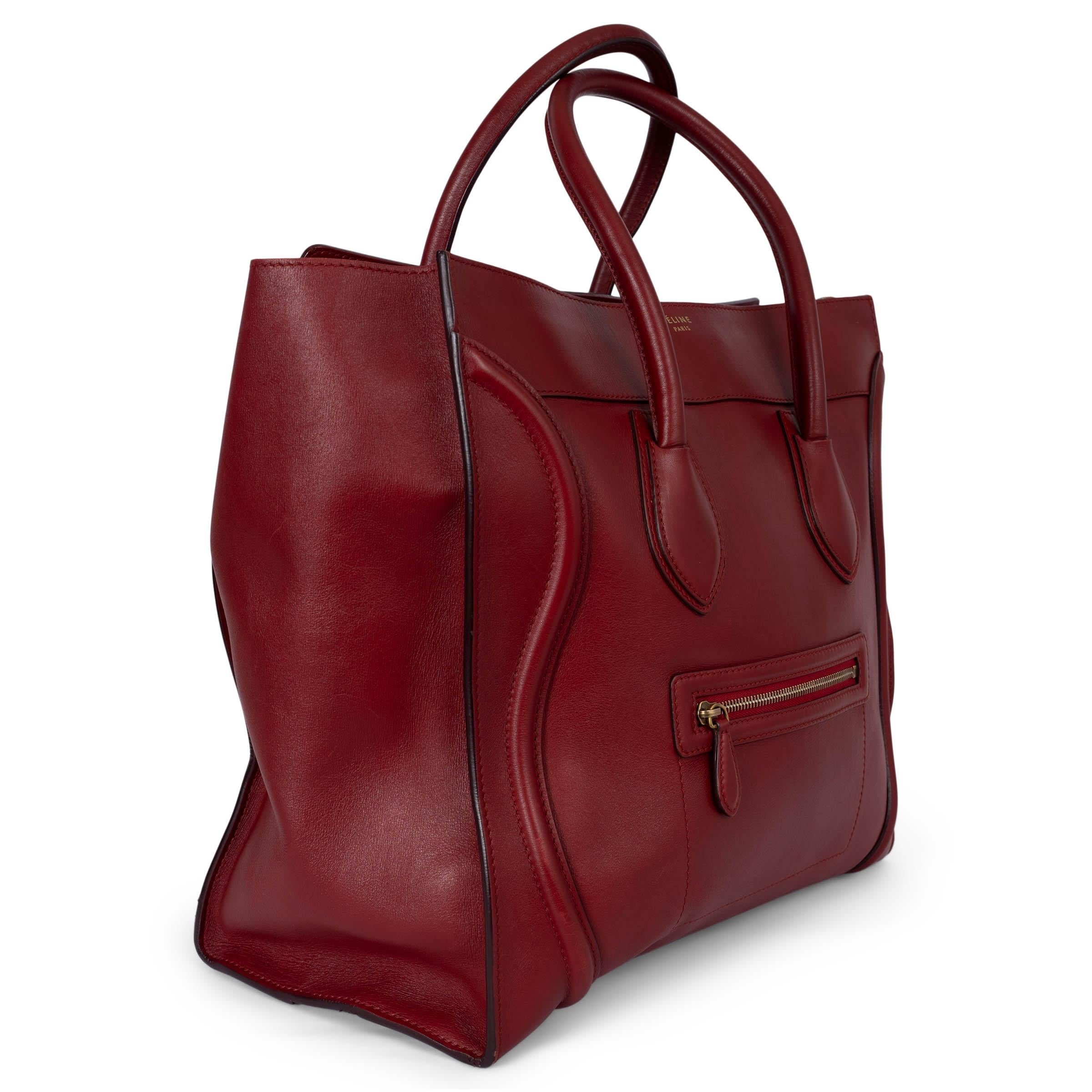 Este bolso mediano 100% auténtico de Céline en piel de becerro Palmelato roja es una pieza llamativa y lujosa, con herrajes en tono dorado antiguo que complementan la rica piel roja. El bolso se abre con una cremallera en la parte superior,