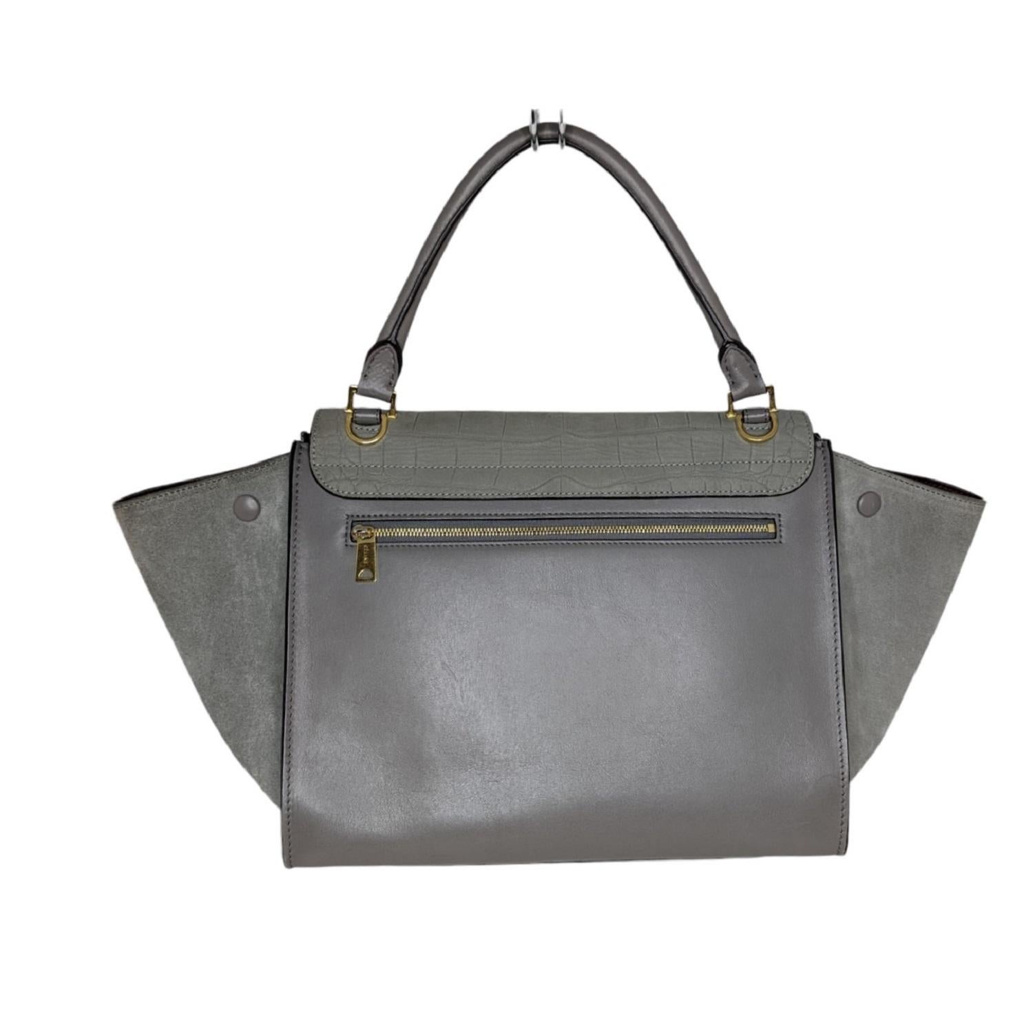 This chic tote is composed of crocodile embossed suede leather, contrasting smooth leather, and brass hardware. This bag features a smooth rolled leather top handle, a smooth leather shoulder strap, expansive suede leather side wings, and a