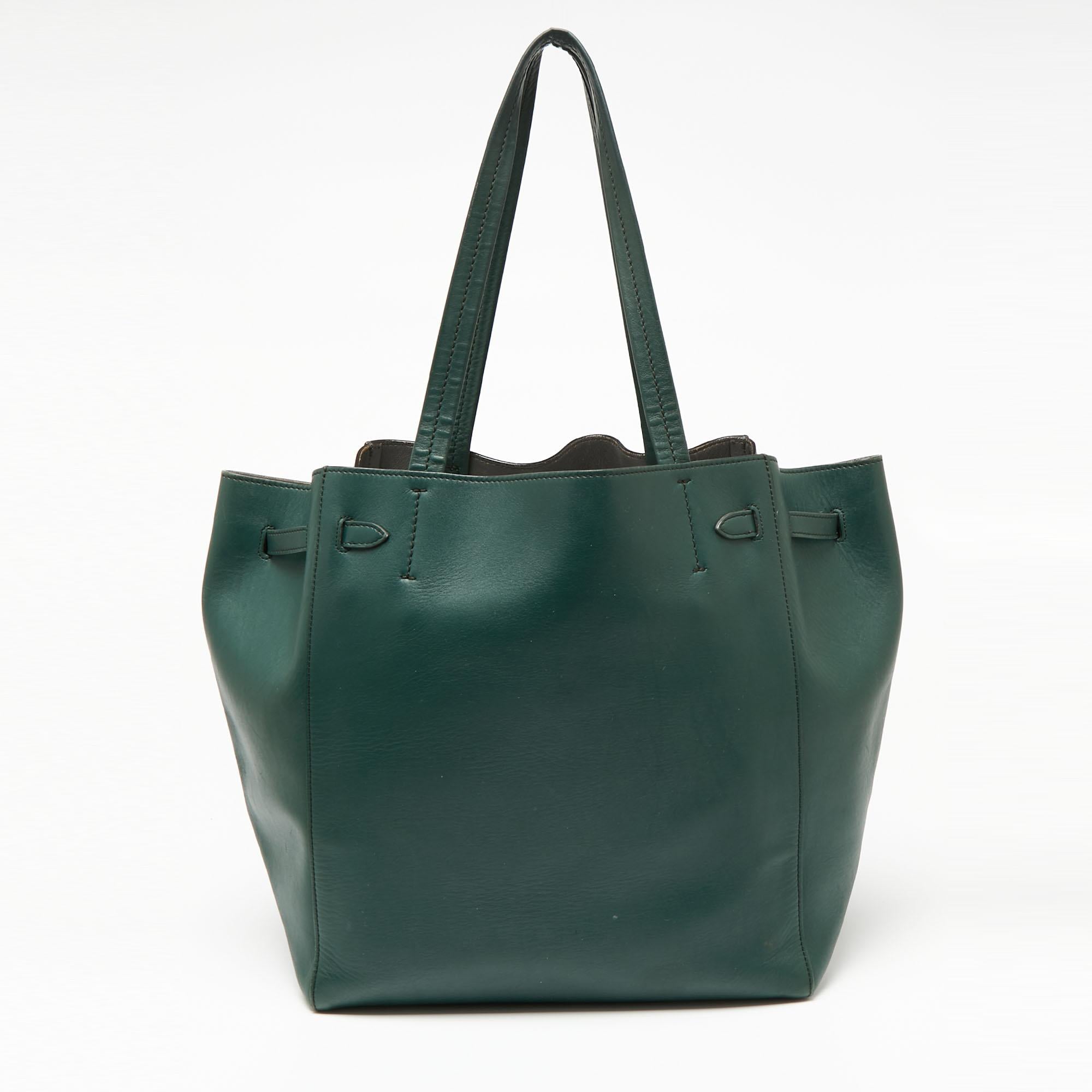This Cabas Phantom tote is from one of the most loved collections from Céline. This tote serves as a fine alternative to carrying all your belongings. Its exterior is in a green tone leather with a tie detail and two handles on top.

