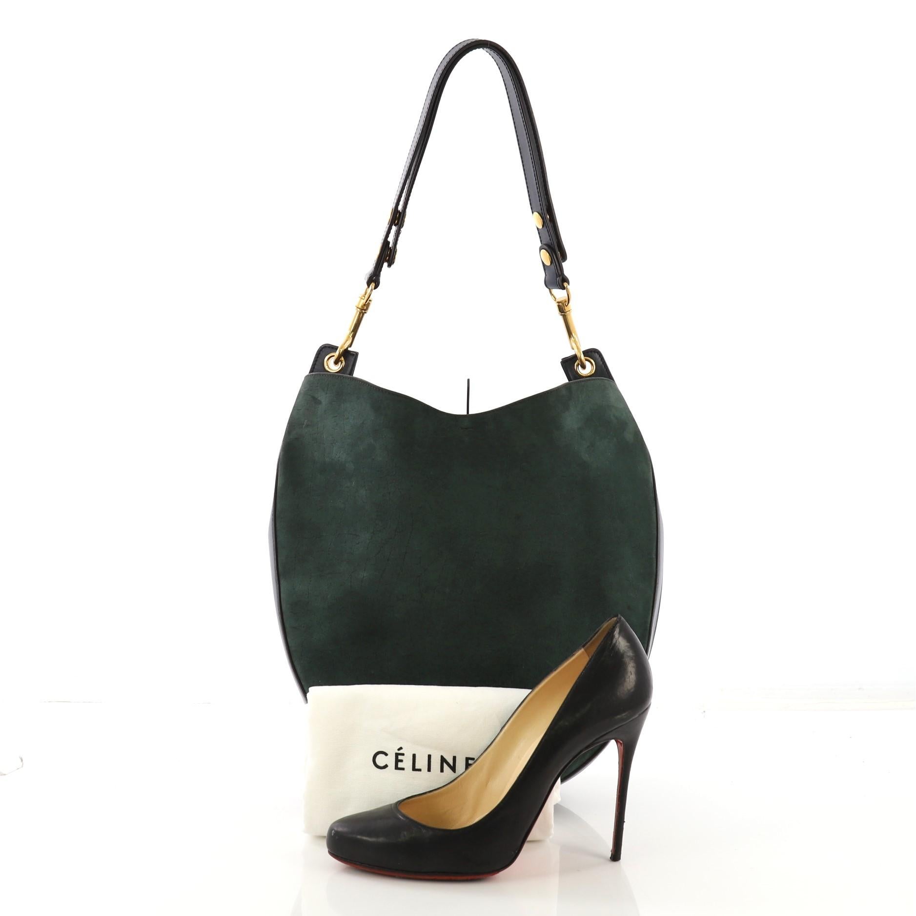 This Celine Hobo NM Suede Medium, crafted from dark green suede and blue leather, features a single adjustable shoulder strap, stamped Celine logo, and aged gold-tone hardware. Its top center leather strap knot closure opens to a blue leather