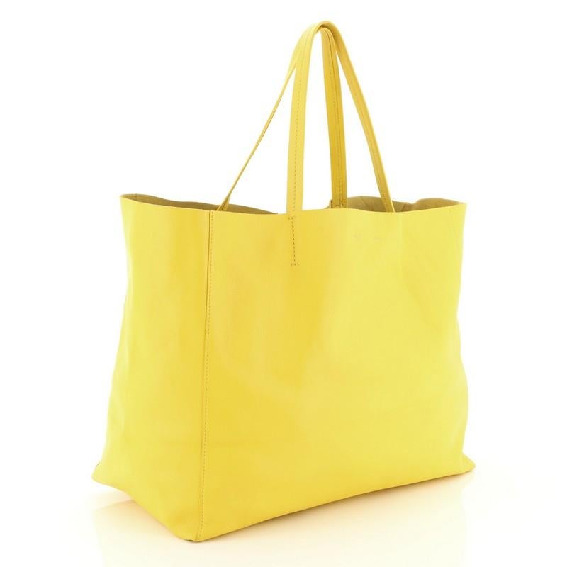 This Celine Horizontal Cabas Tote Leather Large, crafted in yellow leather, features dual flat leather handles, stamped Celine logo at the center, and gold-tone hardware. Its wide open top showcases a yellow raw leather interior with zip pocket.