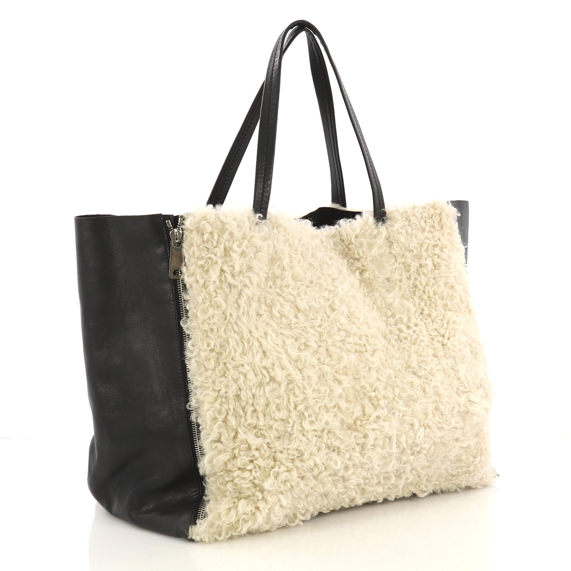 This Celine Horizontal Gusset Cabas Tote Shearling and Leather Large, crafted with off-white shearling and black leather, features dual slim leather handles, front and back zippers that allow bag to expand and silver-tone hardware. It opens to a