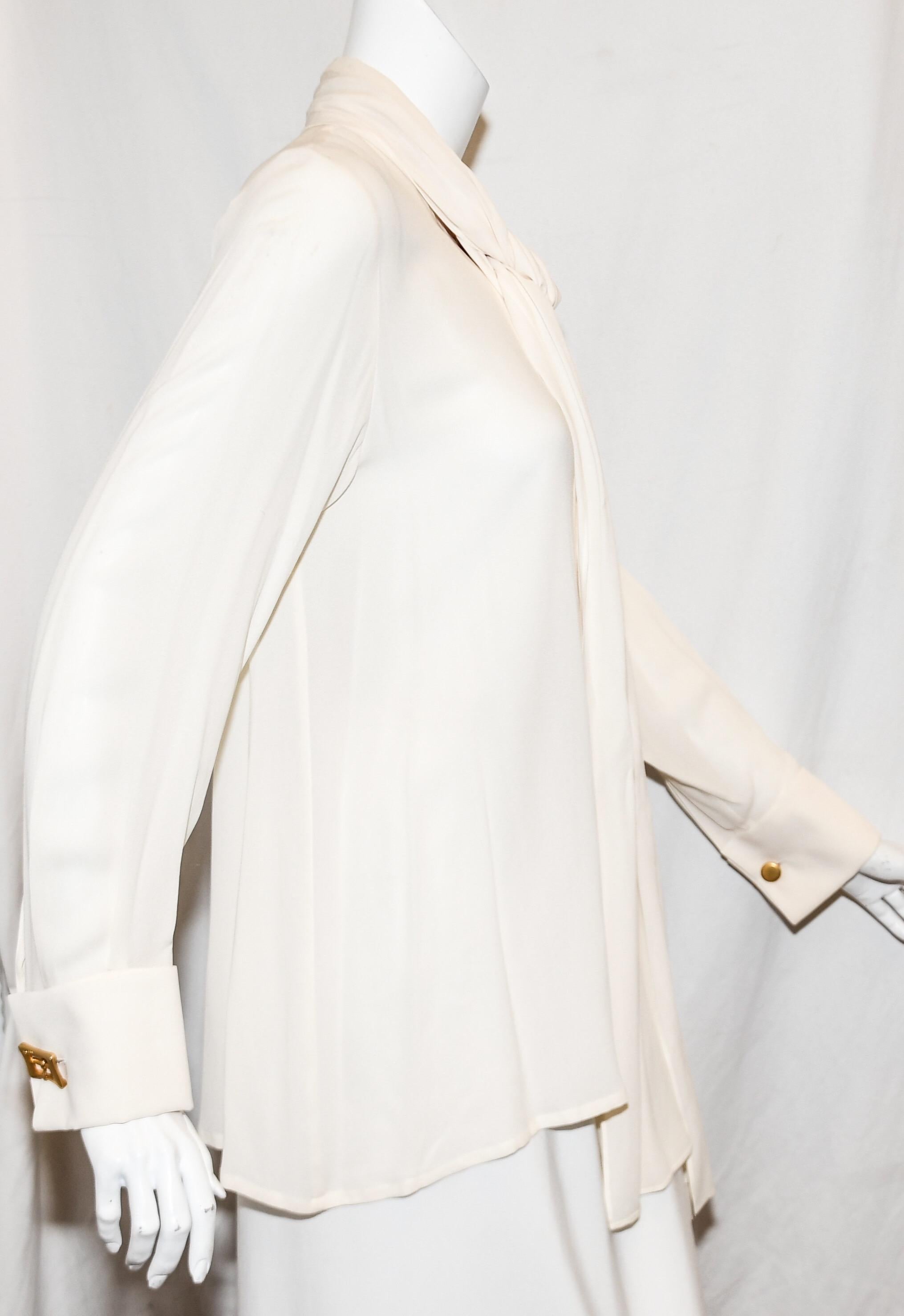 Celine ivory 100% silk blouse includes two long straps from the collar that can be tied around collar in a bow, left hanging or as a cravat.  The long sleeves contain up cuffs that are accentuated with square Celine logo cuff links.  This top is not