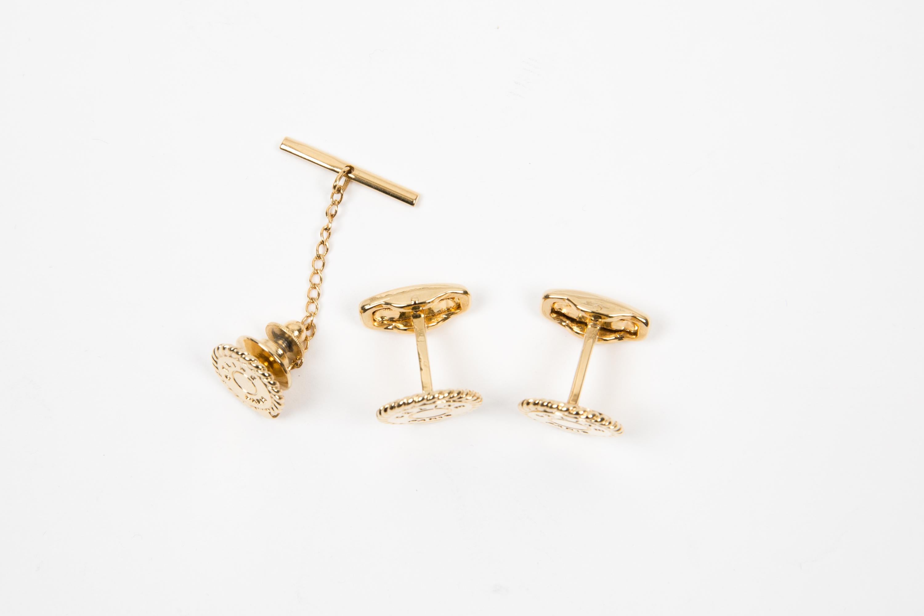 Ensemble de boutons de manchette et de maillons de cravate logo Celine en métal doré présentant une forme ronde, un contour en maillons de chaîne, un logo central piqué. Elles sont livrées par paire + un accessoire de cravate. 
Elles sont livrées