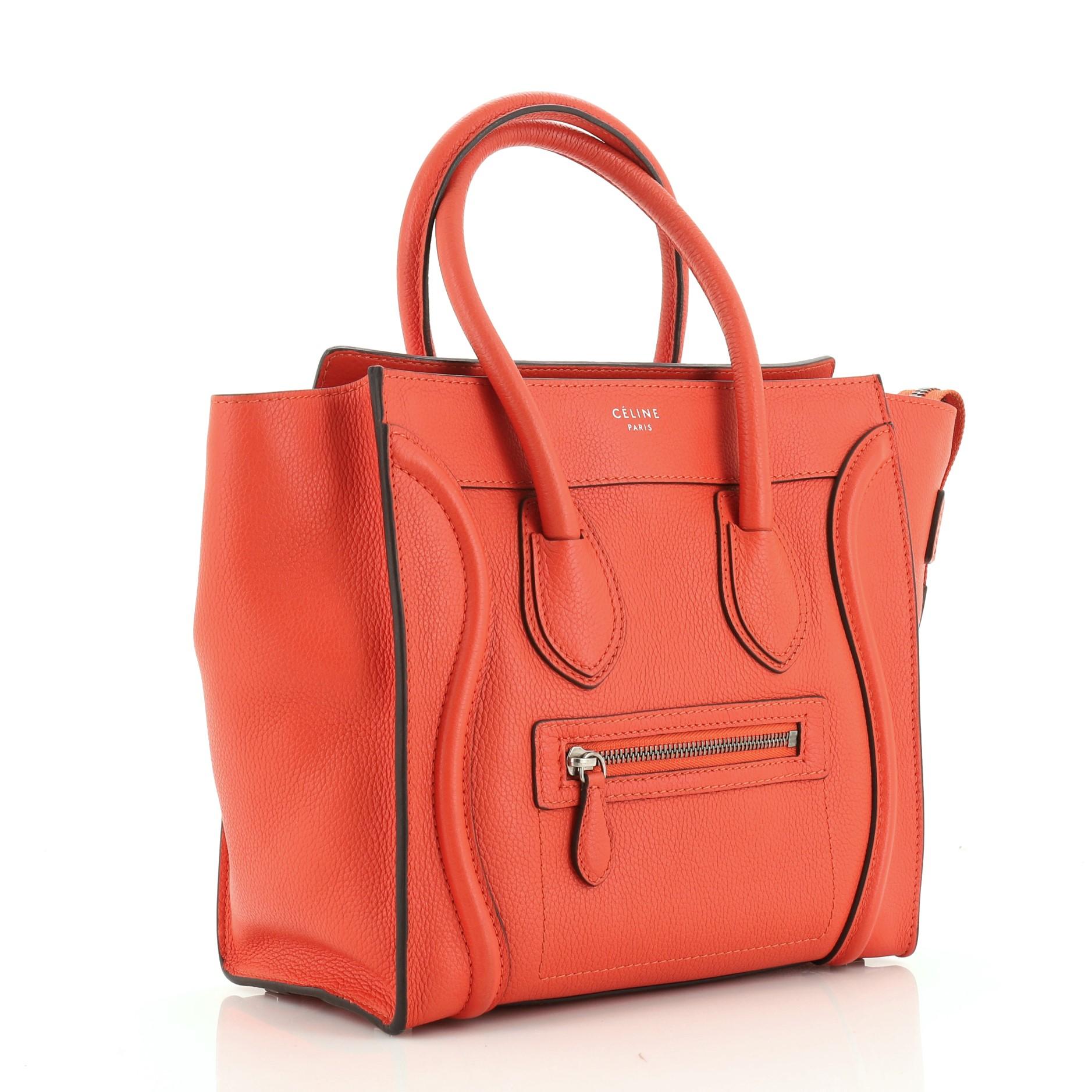 This Celine Luggage Bag Grainy Leather Micro, crafted from orange grainy leather, features dual rolled handles, exterior front zip pocket, and silver-tone hardware. Its zip closure opens to an orange suede interior with side zip and slip pockets.