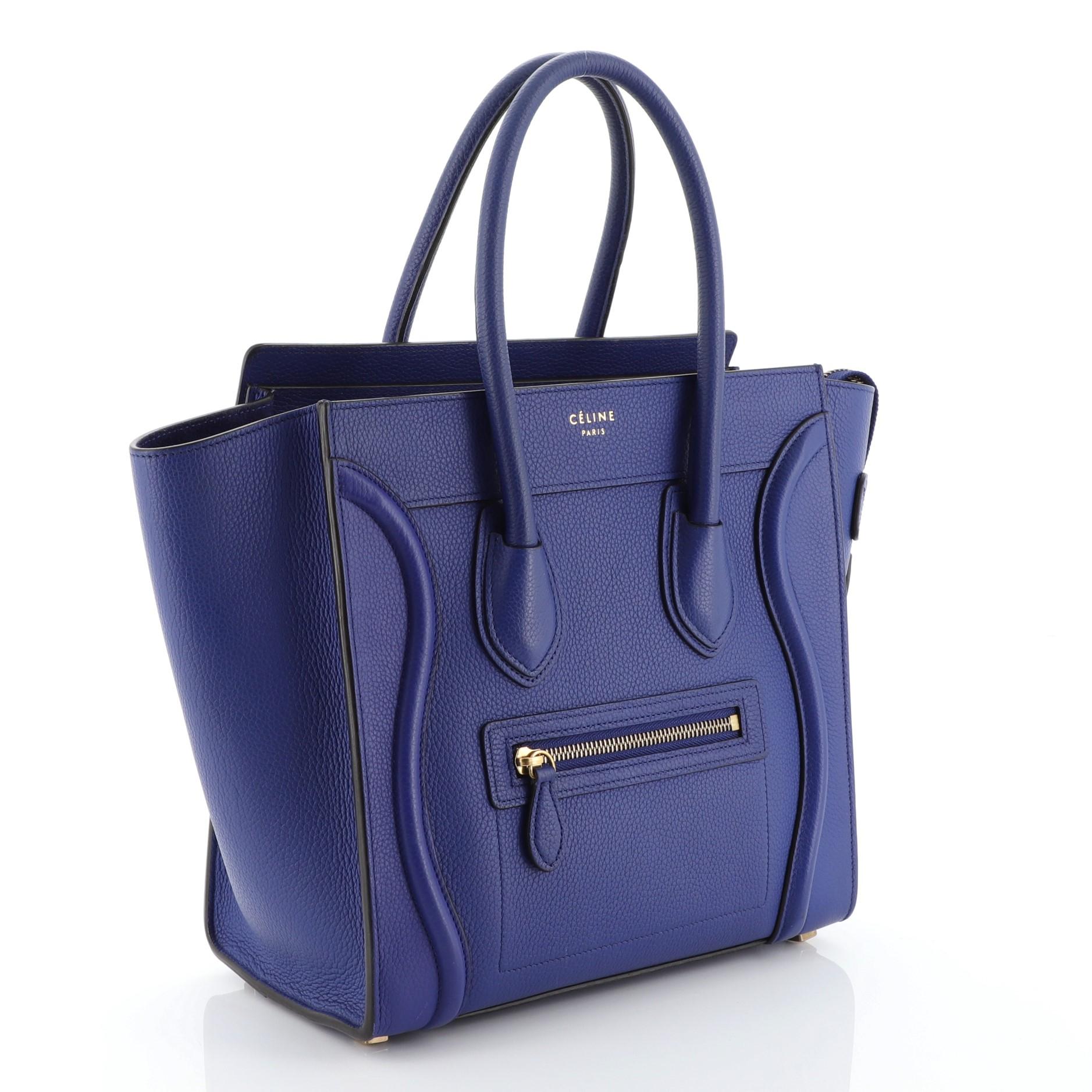 This Celine Luggage Handbag Grainy Leather Micro, crafted from blue grainy leather, features dual rolled handles, exterior front zip pocket, and aged gold-tone hardware. Its zip closure opens to a blue suede interior with side zip and slip pockets.