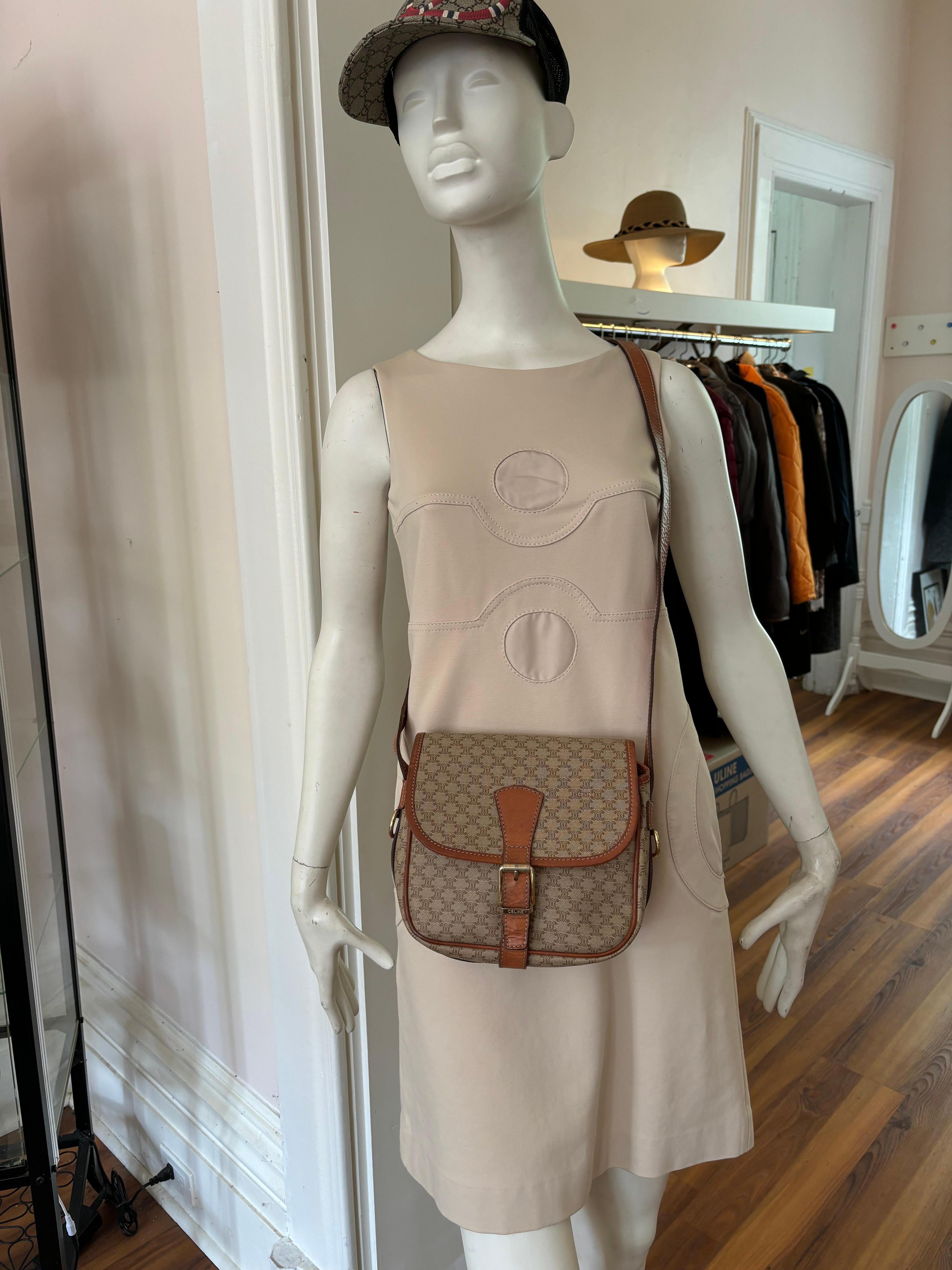 Offered is a Celine Macadam Triomphe in PVC and leather in beige with tan leather accents, including the crossbody strap and wrap around surround.
The hardware is gold colored , and although there is a front buckle, opening and closure is by a