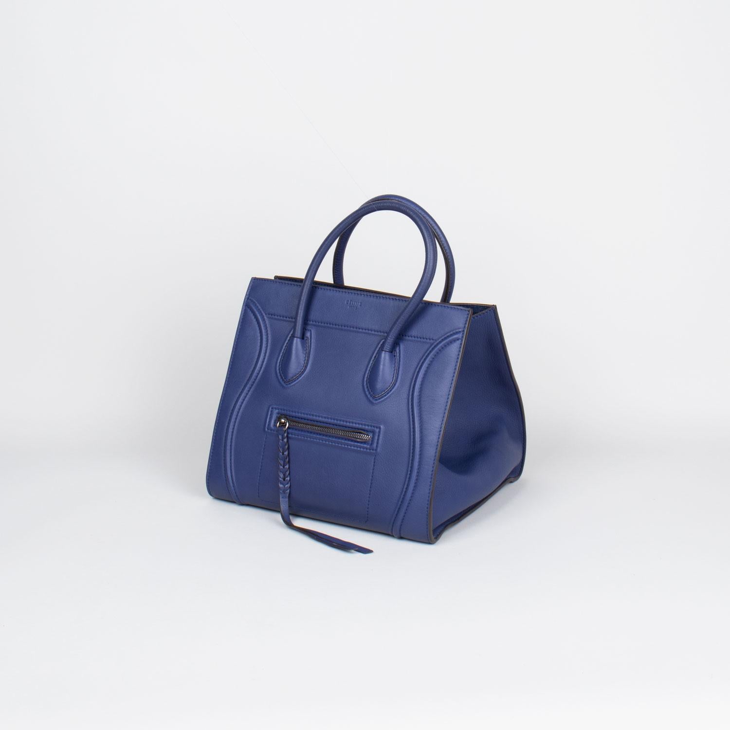 From the Winter 2014 Collection by Phoebe Philo. Navy drummed calfskin leather Céline Medium Luggage Phantom tote with 

– Silver-tone hardware
– Dual rolled top handles
– Zip pocket at front
– Tonal trim throughout exterior
– tonal suede lining,
