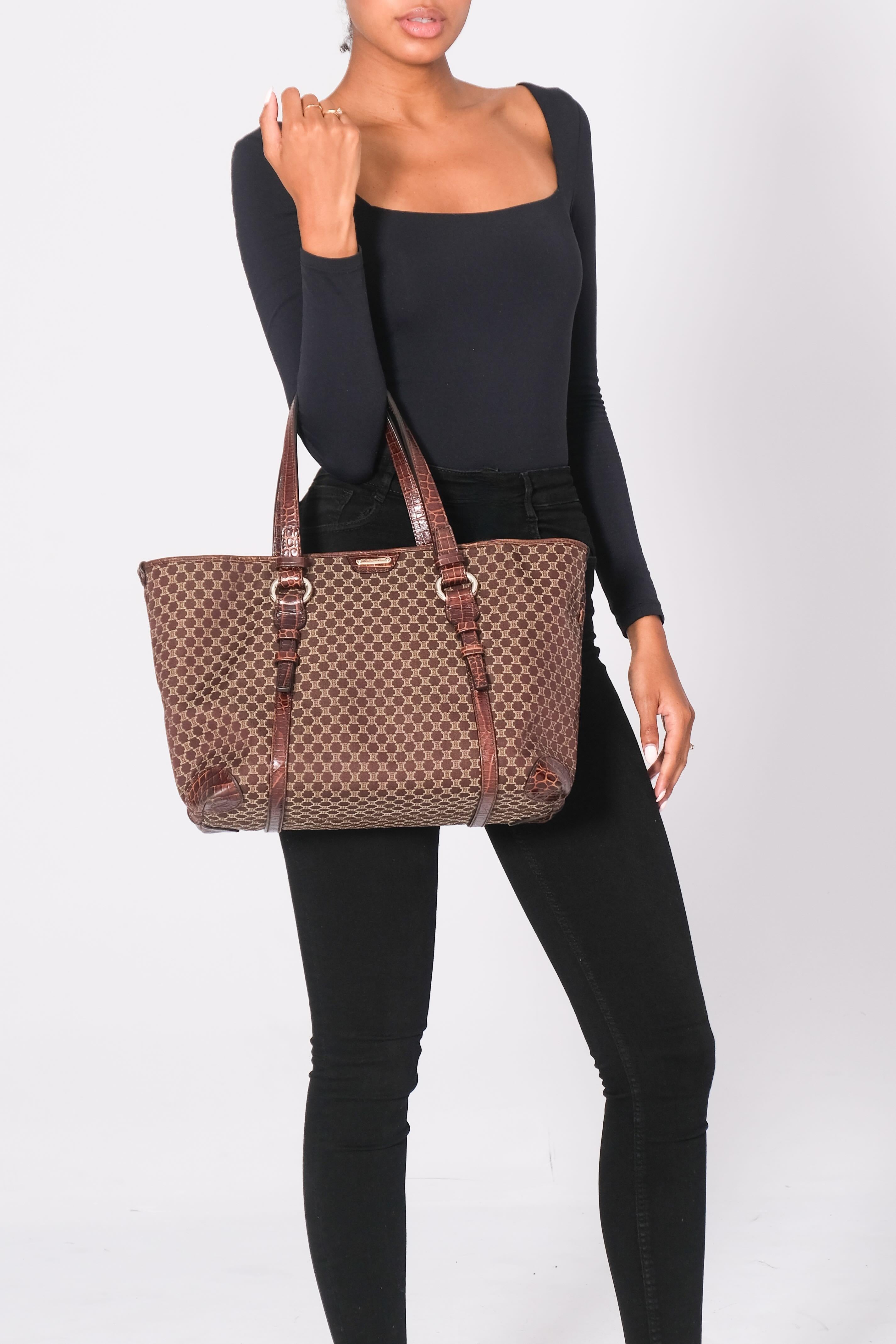 The Celine tote bag is made of brown canvas with a Jacquard weave, featuring the signature vintage Celine Macadam monogram print. The bag includes dual flat leather top handles and brown croc-embossed leather details, including the corners. The