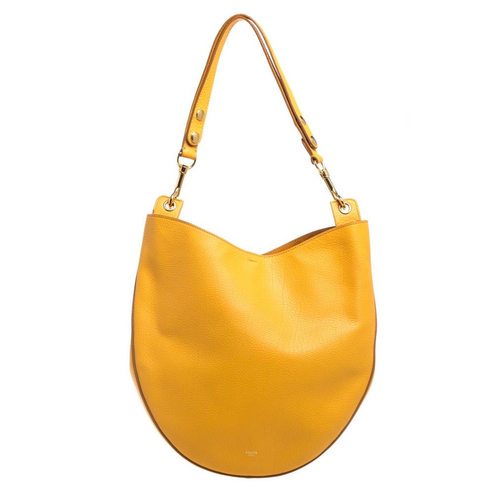This classic Celine hobo is a must-have! Crafted from smooth leather in a mustard hue and brushed with gold-tone hardware, it features a flat shoulder strap and a suede & leather-lined interior with one zippered pouch. It has a sleek silhouette that
