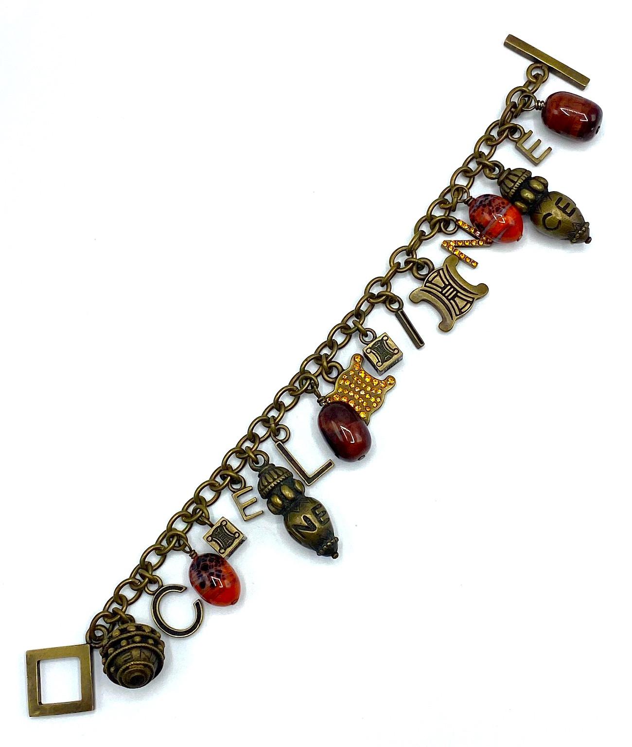Un magnifique bracelet à breloques entièrement chargé de Céline des années 1990. Il a une finition patinée bronze antique et comporte 17 breloques. Six des breloques sont des lettres qui épellent Céline. Les quatre breloques sont des perles de verre