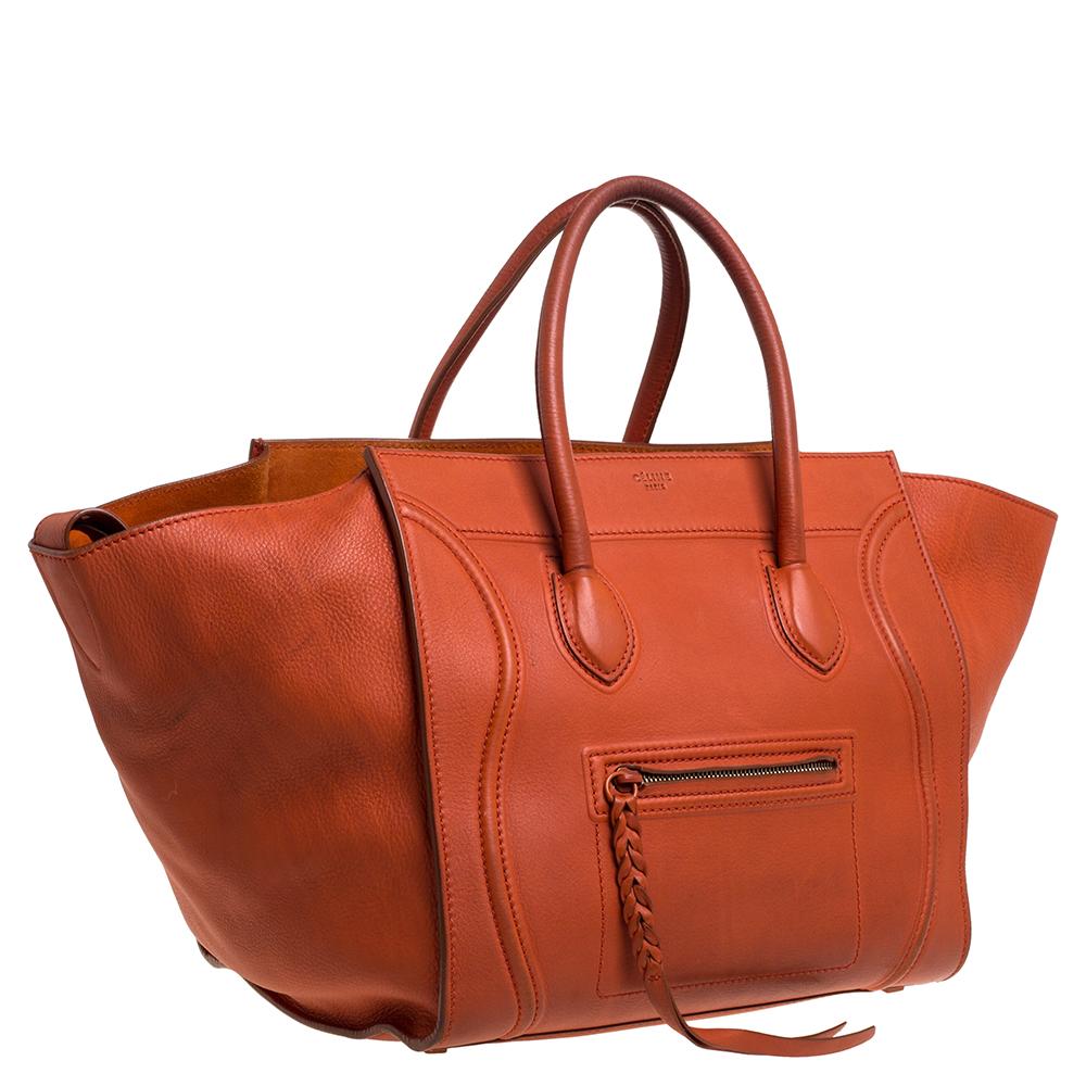 Celine released the Phantom as a newer version of its successful Luggage model. Unlike the Luggage toes, the Phantom has an open-top, wider wingspans, and a braided zipper pull. We have here the one in leather. It has two top handles, an orange
