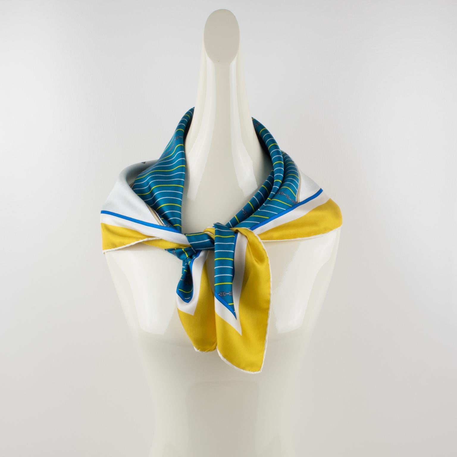 Elegant silk scarf by Celine Paris. A geometric print pattern with an equestrian design of riding helmet, whip, and gloves in a combination of bright blue, white, and yellow colors with a yellow and white border. Signed Celine Paris in the bottom