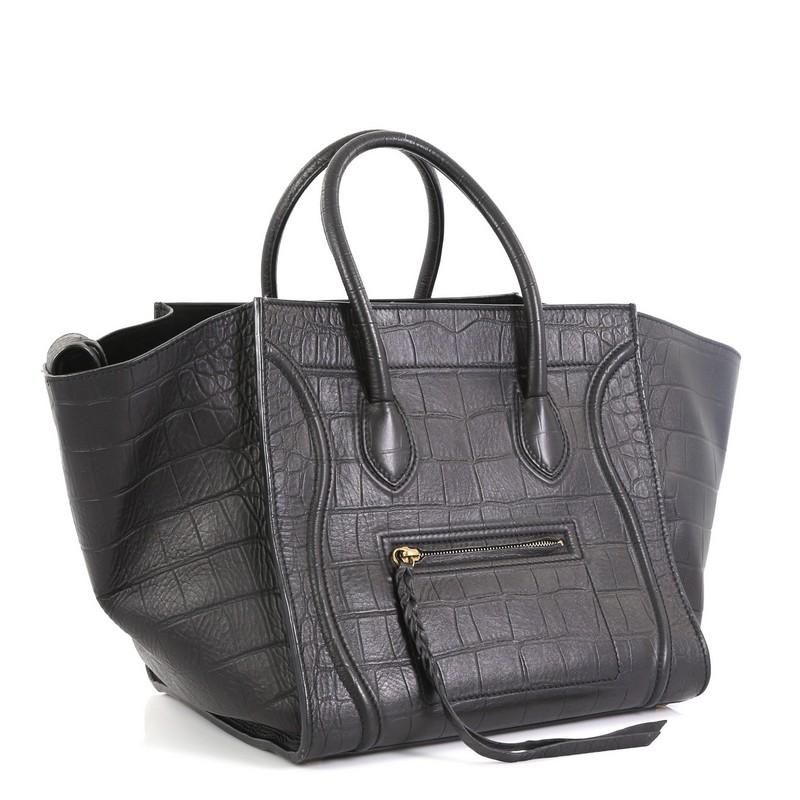 This Celine Phantom Bag Crocodile Embossed Leather Medium, crafted from black crocodile embossed leather, features dual rolled handles, exterior front zip pocket, and aged-tone hardware. It opens to a black suede interior with zip pocket.