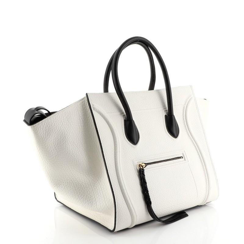 This Celine Phantom Bag Grainy Leather Medium, crafted from white grainy leather, features dual rolled handles, exterior front zip pocket, protective base studs, and aged gold-tone hardware. It opens to a neutral suede interior with side zip pocket.