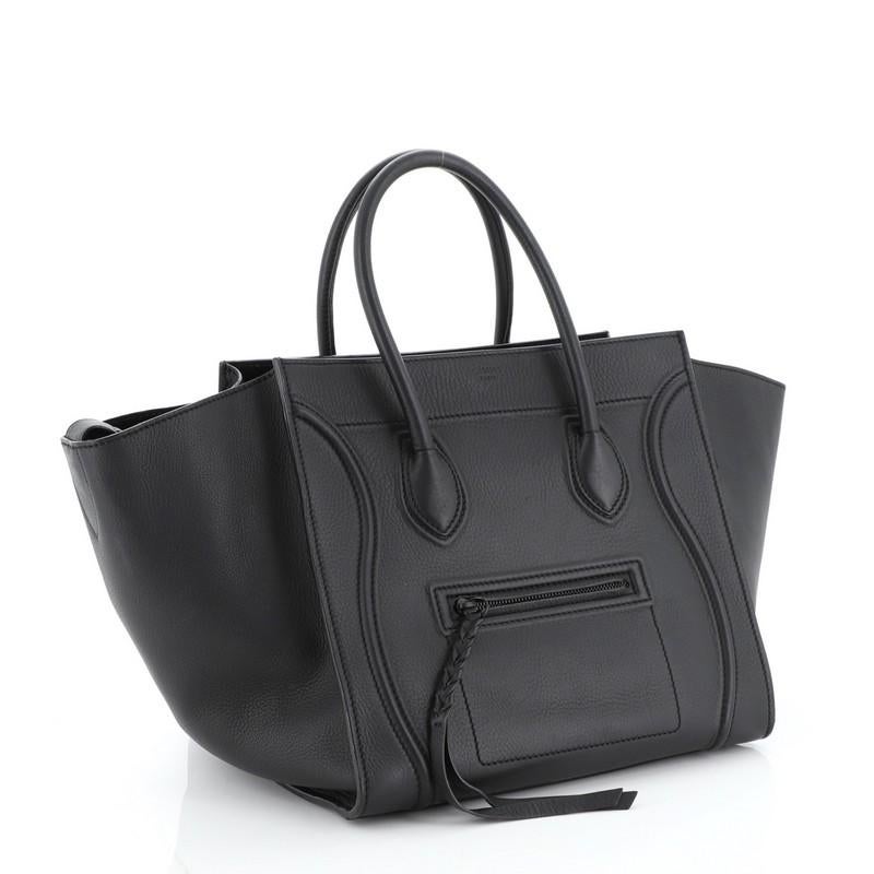This Celine Phantom Bag Grainy Leather Medium, crafted from black grainy leather, features dual rolled handles, exterior front zip pocket, protective base studs, and black-tone hardware. It opens to a black suede interior with side zip pocket.