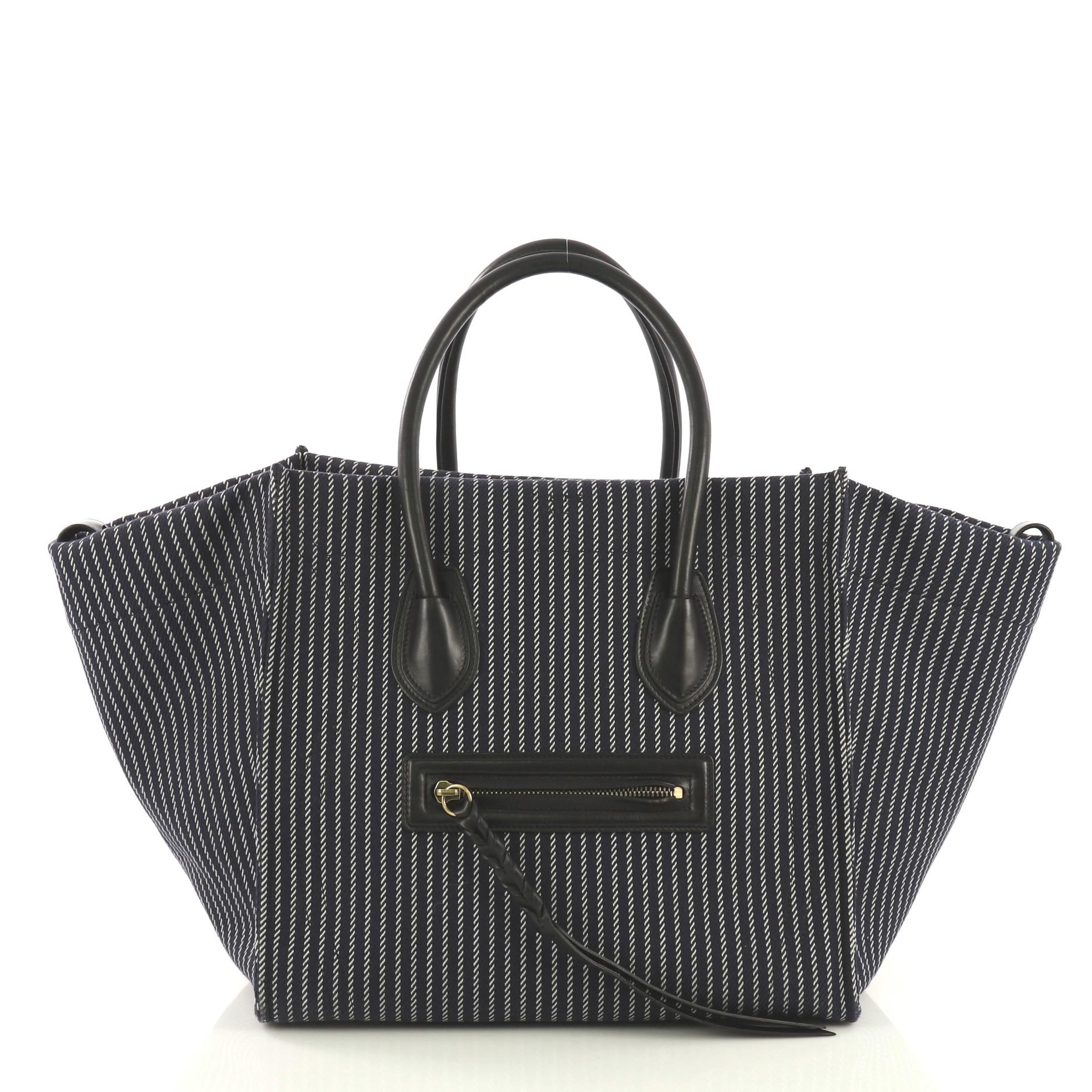 This Celine Phantom Handbag Canvas Medium, crafted from navy blue and white striped canvas, features dual rolled leather handles, exterior front pocket, and aged gold-tone hardware. It opens to a navy striped canvas interior with side zip pocket.