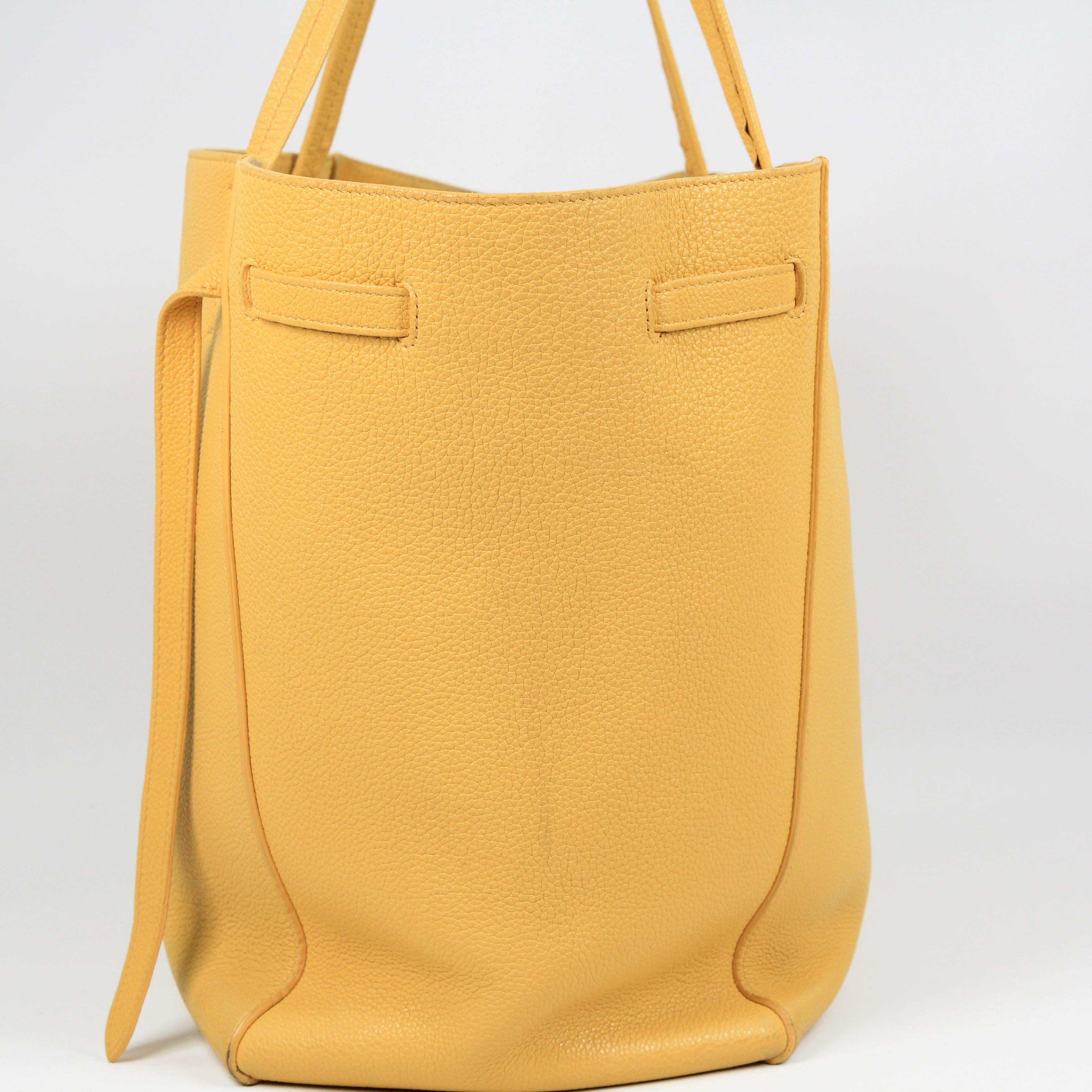 This small Phantom Cabas Tie tote has a belted cinch at the sides with ties that hang in the front of the bag or that can be tied up in a bow. Crafted out of gorgeous yellow drummed calfskin leather, this bag reminds us the Celine loves their high