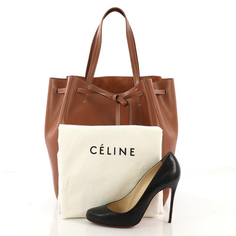 This Celine Phantom Tie Cabas Tassel Tote Leather Medium, crafted from brown leather, features dual flat tall handles and stamped Celine logo. Its drawstring tie closure opens to a brown raw leather interior with side zip and slip pockets. **Note: