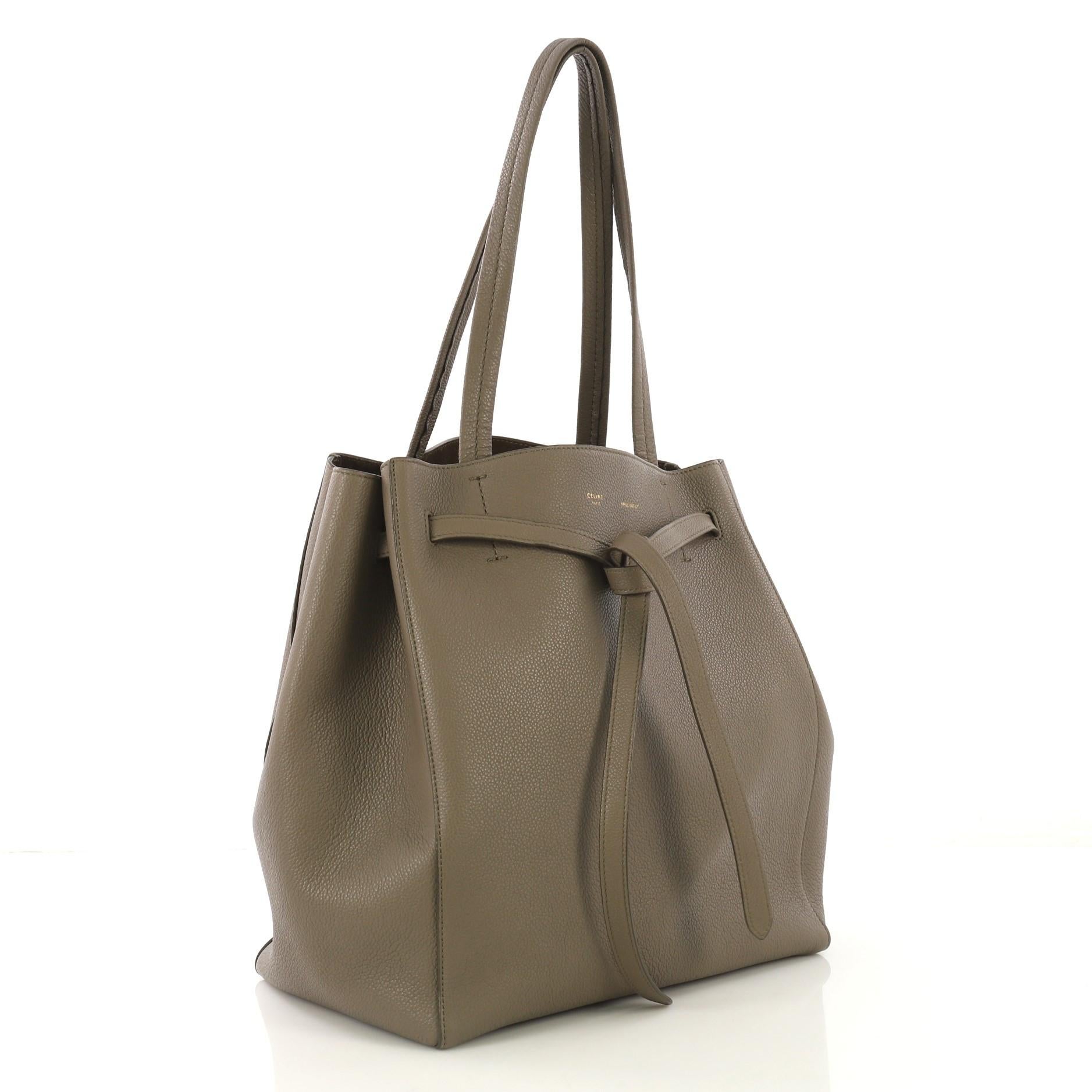 This Celine Phantom Tie Cabas Tote Leather Small, crafted from taupe leather, features dual flat tall handles, stamped Celine logo, and gold-tone hardware. Its drawstring tie closure opens to a brown suede interior with side zip pocket. 

Estimated