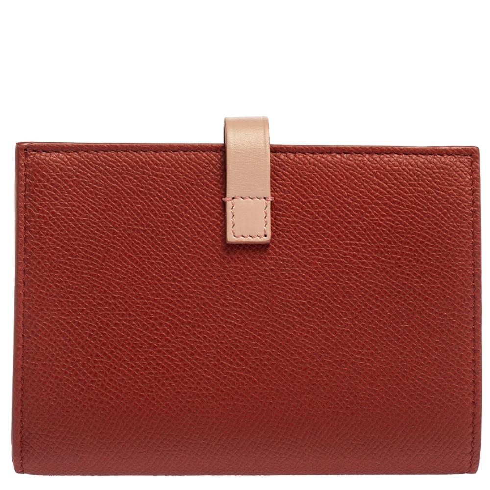 This chic wallet is crafted of lovely grained leather in red. The creation has a frontal flap with a light pink strap snap closure that opens to a compact partitioned leather interior with two panels of card slots and a zipper compartment. This