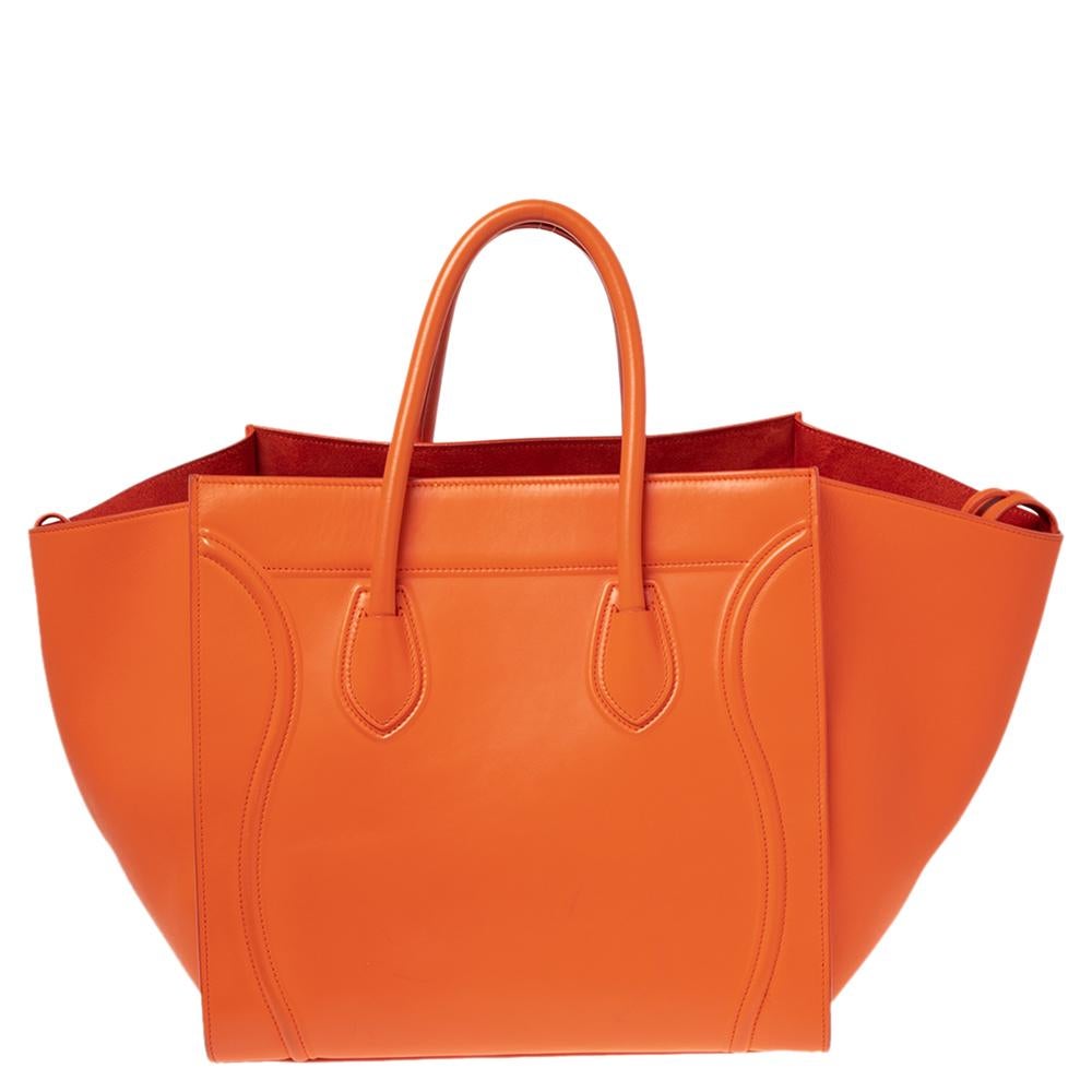 Celine released the Phantom as a newer version of their successful Luggage model. Unlike the Luggage toes, the Phantom has an open top, wider wingspans, and a braided zipper pull. We have here the one in leather. It has two top handles, an orange