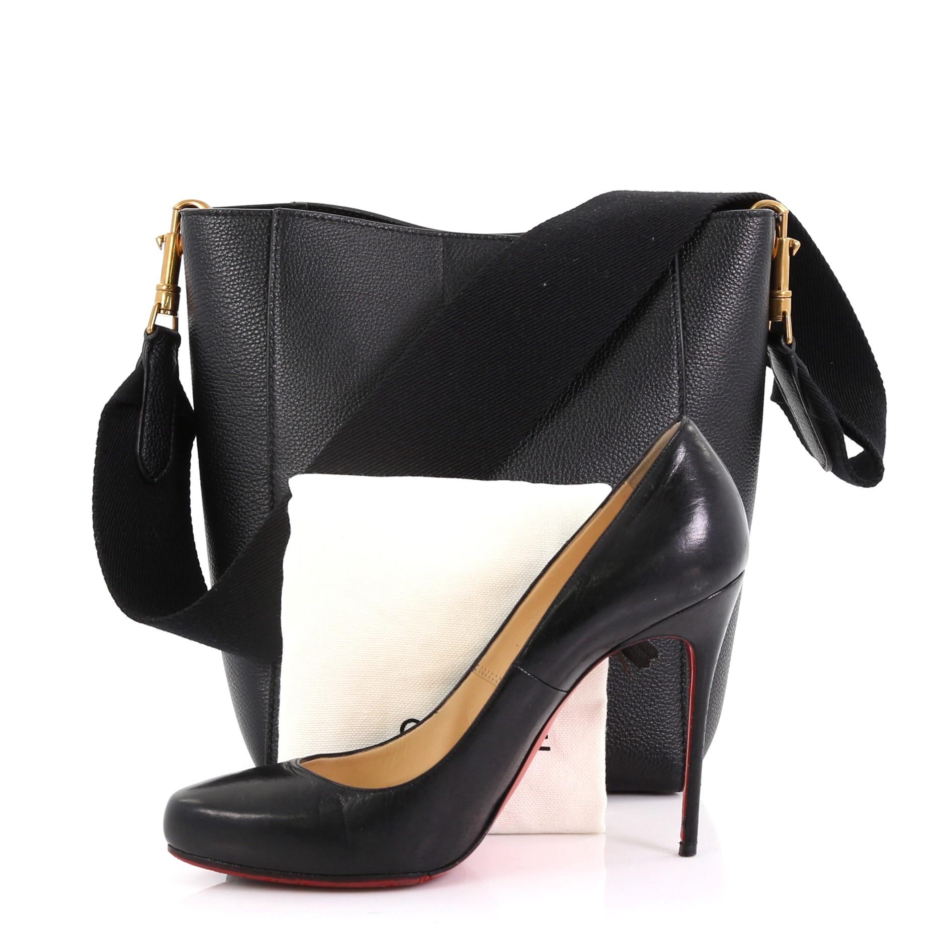 This Celine Sangle Seau Bag Calfskin Small, crafted from black leather, features a canvas shoulder strap and gold-tone hardware. Its clasp-hook closure opens to a black suede interior with side zip and slip pockets. **Note: Shoe photographed is used