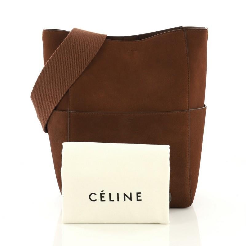 This Celine Sangle Seau Bag Suede Large, crafted from brown suede, features a flat shoulder strap, exterior slip pockets and gold-tone hardware. Its clasp-hook closure opens to a brown leather interior with side zip and slip pockets. 

Estimated