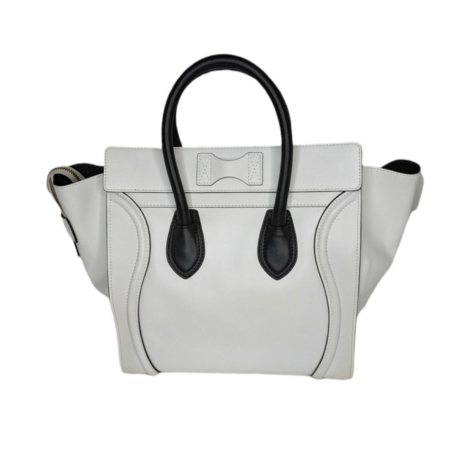 This stylish tote bag is crafted of rich white calfskin leather. The bag features rolled black leather top handles, and the iconic Celine leather scroll trim in white on the front. The overextended top zipper opens the bag to a smooth black leather