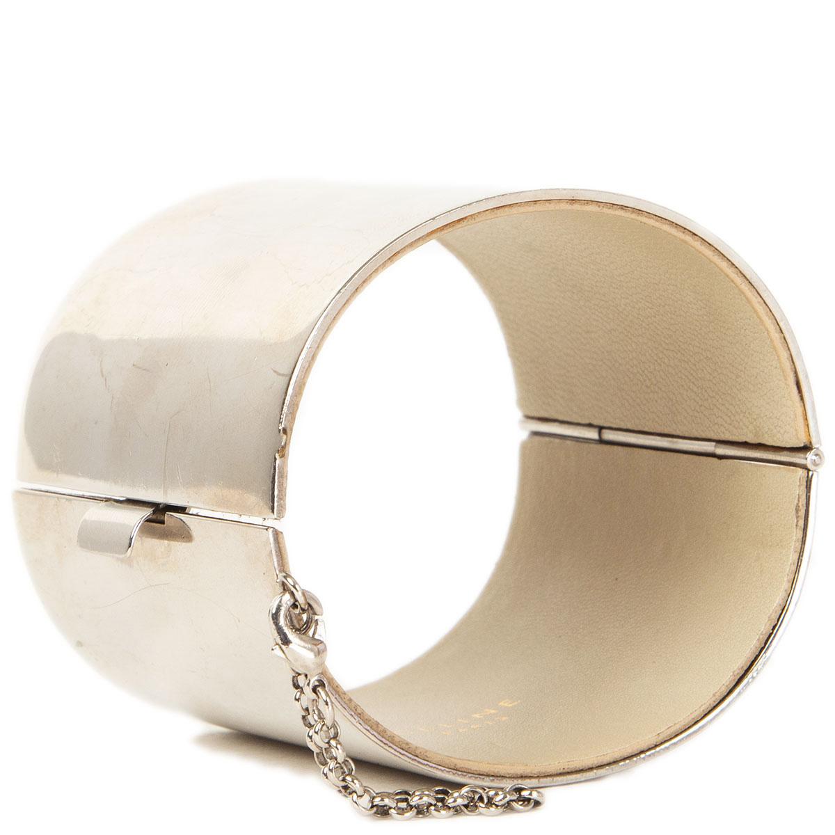 100% authentic Céline wide manchette cuff bracelet in silver-tone metal lined with light taupe lambskin. Has been worn and the little chain detail is broken on one side and now only attached to one side. Bracelet shows some wear and scratches