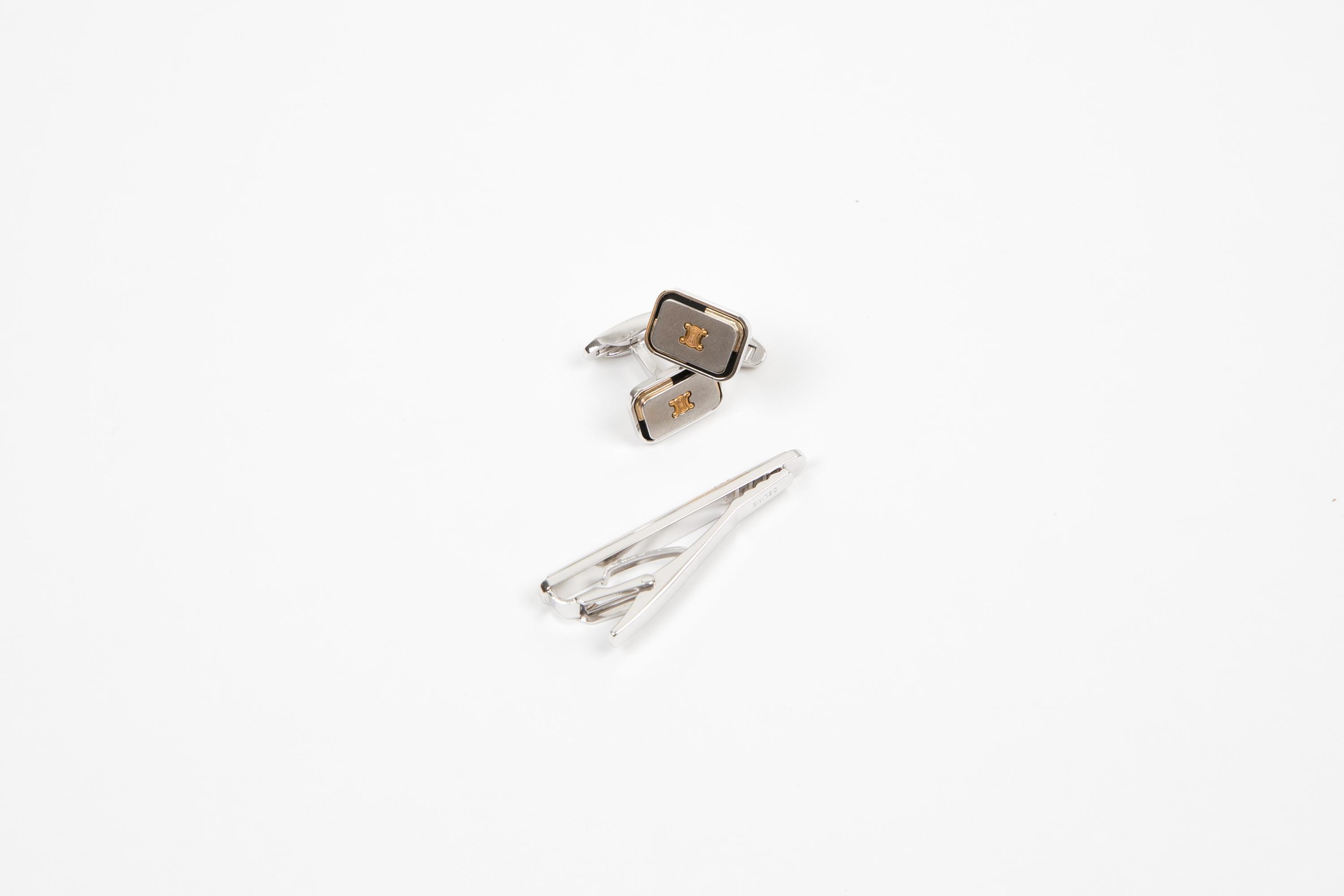 Celine Silver-tone “Triomphe” cuff-links and tie logo link set featuring a silver-tone textured ground, a gold-tone front “Triomphe” design and a black and gold-tone outline, a rectangular shape. They come as a pair + a tie accessory. 
Delivered in