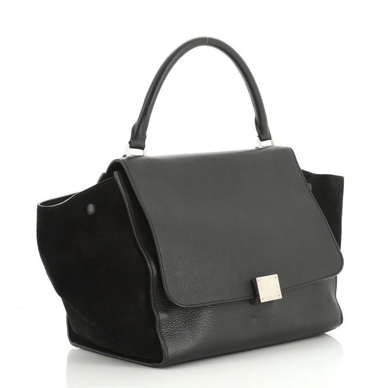 This Celine Trapeze Bag Leather Medium, crafted from black leather, features a rolled leather handle, exterior back zip pocket, and silver-tone hardware. Its square flip-lock and zip closure opens to a black leather interior with slip pockets.