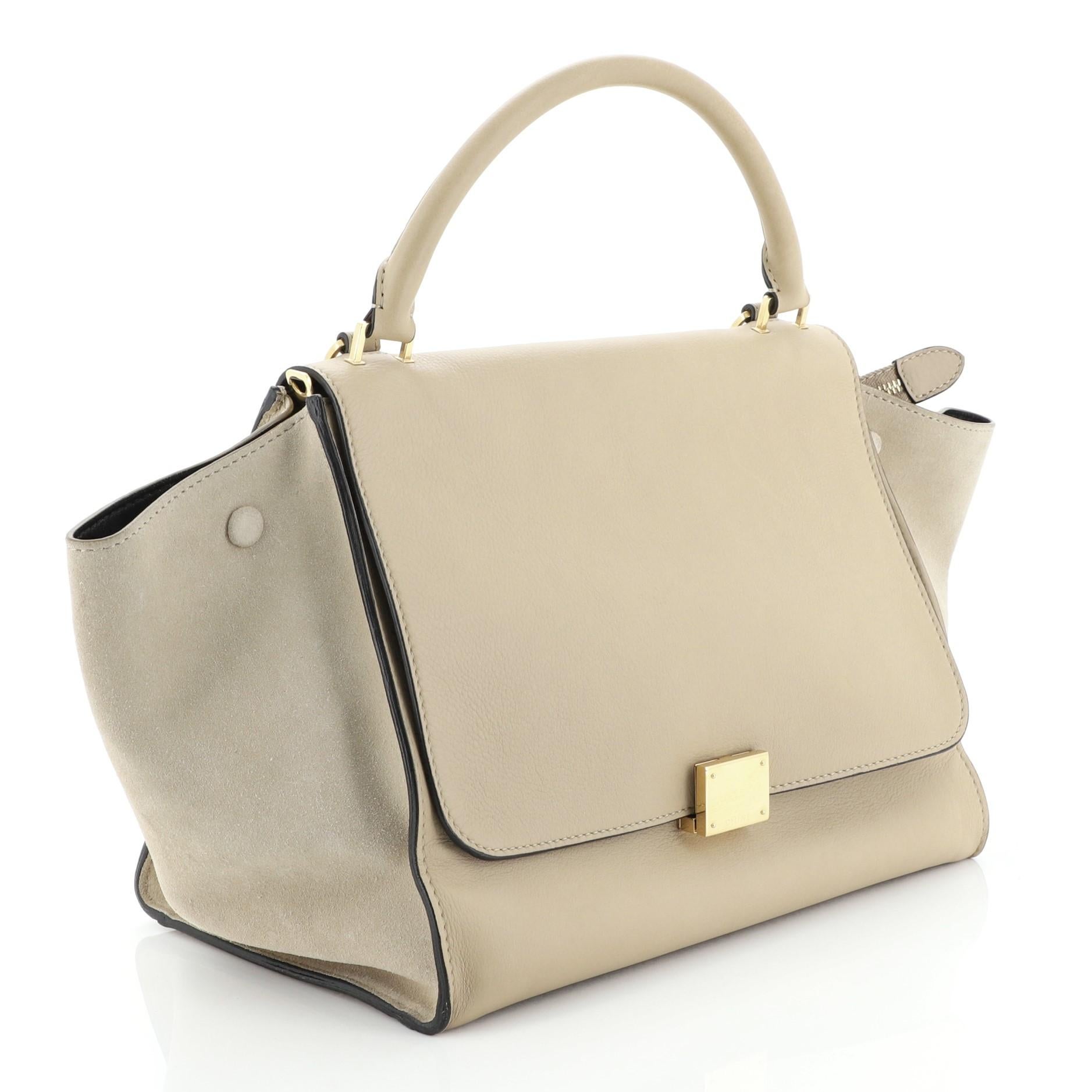 This Celine Trapeze Bag Leather Medium, crafted from neutral leather, features a rolled leather handle, exterior back zip pocket, and gold-tone hardware. Its square flip-lock and zip closure opens to a black leather interior with slip pockets.