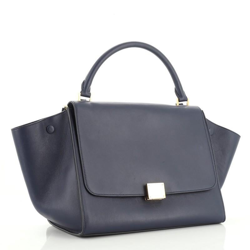 This Celine Trapeze Bag Leather Medium, crafted from blue leather, features a rolled leather handle, exterior back zip pocket, and gold-tone hardware. Its square flip-lock and zip closure opens to a blue suede interior with slip pockets. 

Estimated