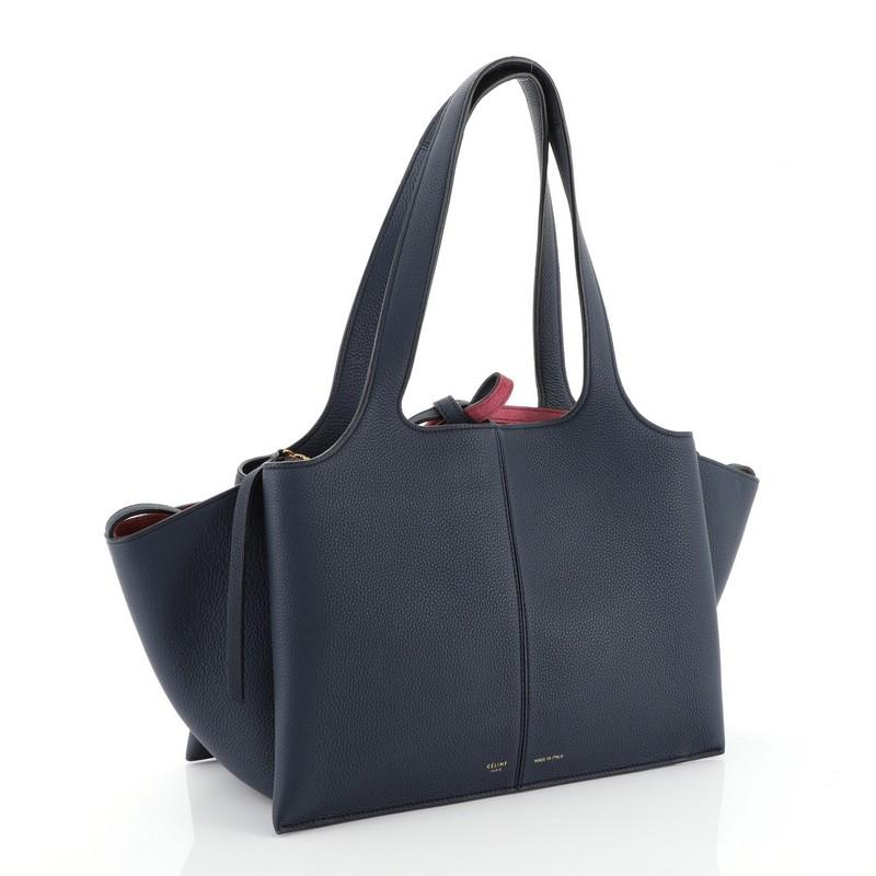 This Celine Tri-Fold Shoulder Bag Grained Calfskin Small, crafted from blue grained calfskin leather, features dual flat leather handles, expandable side wings, and gold-tone hardware. It opens to a red suede interior with side slip pockets.