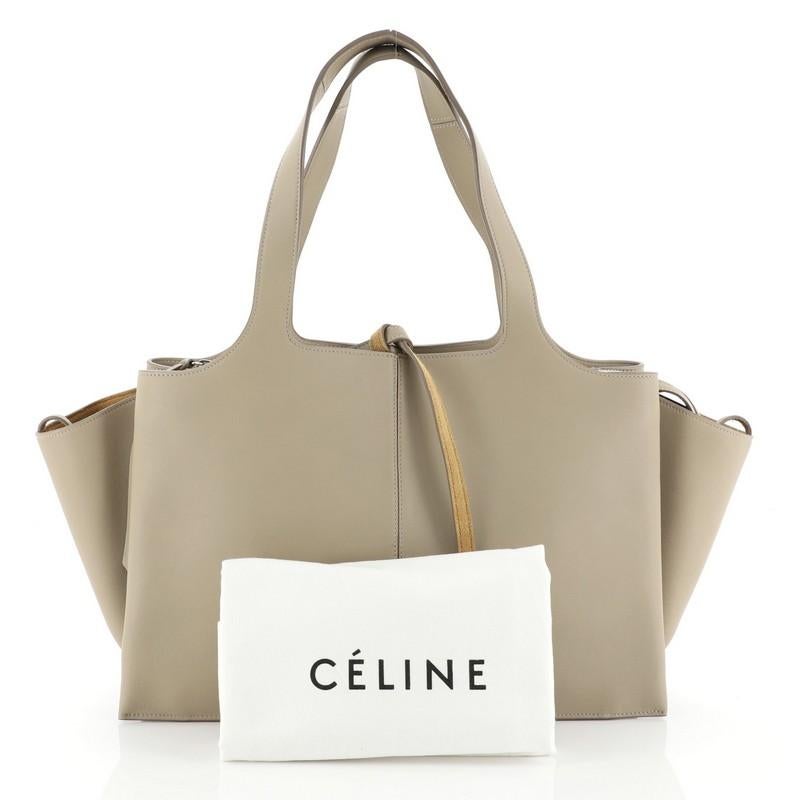 This Celine Tri-Fold Shoulder Bag Smooth Calfskin Medium, crafted from neutral smooth calfskin leather, features dual flat leather handles, two open compartments, expandable side wings and silver-tone hardware. Its zip closure opens to a brown suede